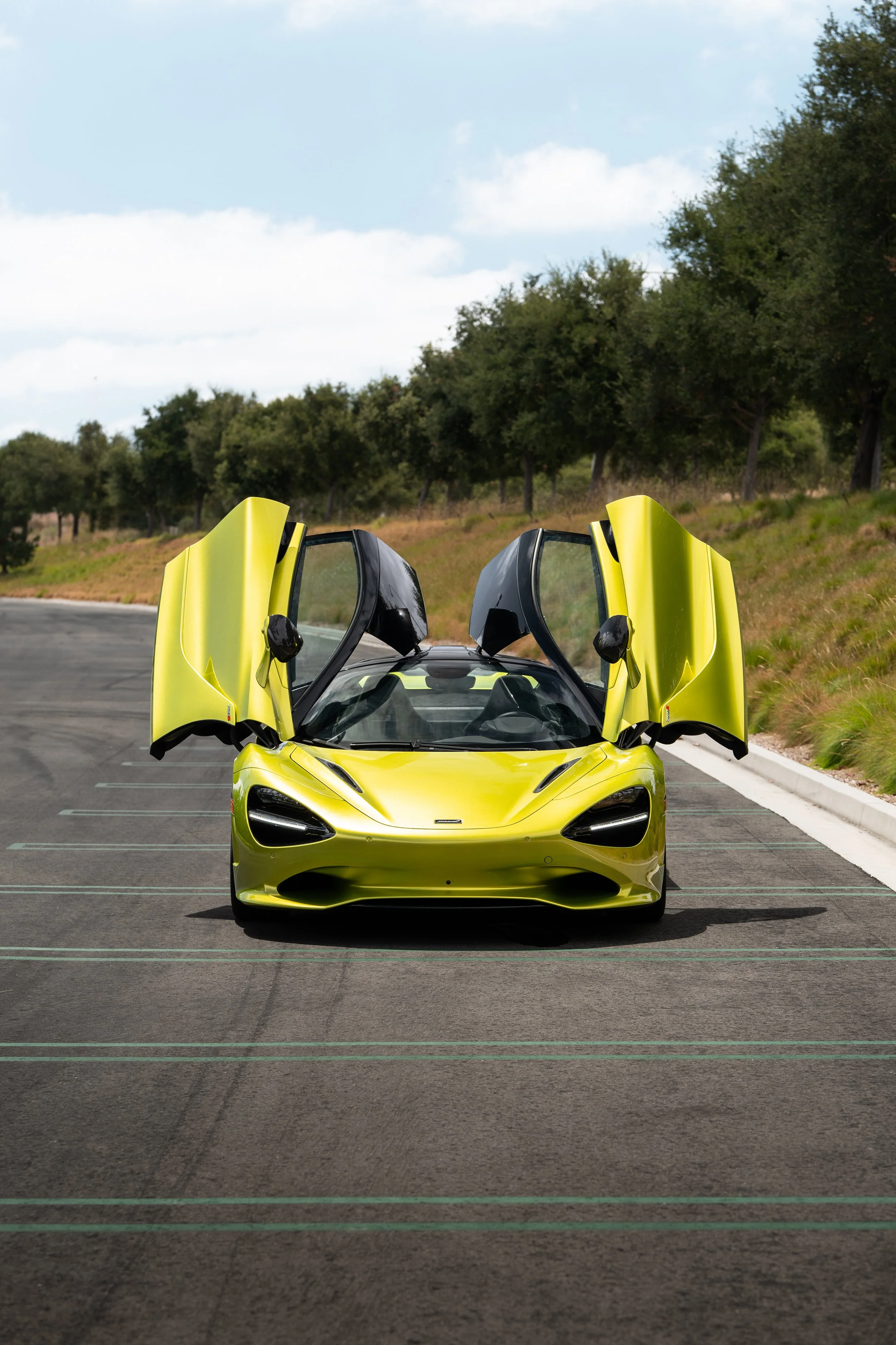 Front view of a lime-green McLaren supercar with both dihedral doors raised, parked outdoors.
