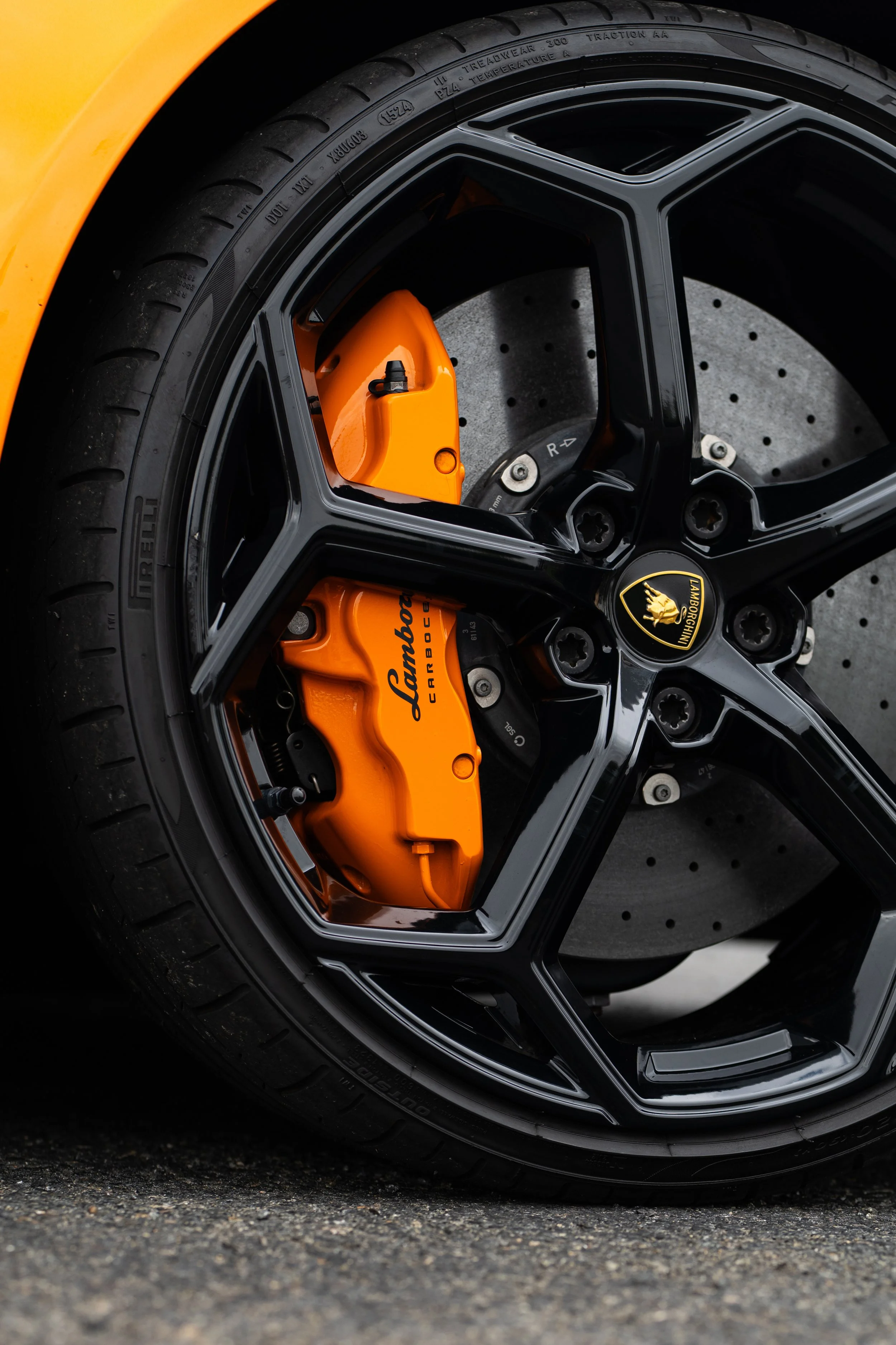 Close-up of an orange Lamborghini brake caliper, drilled brake rotor, and black alloy wheel.