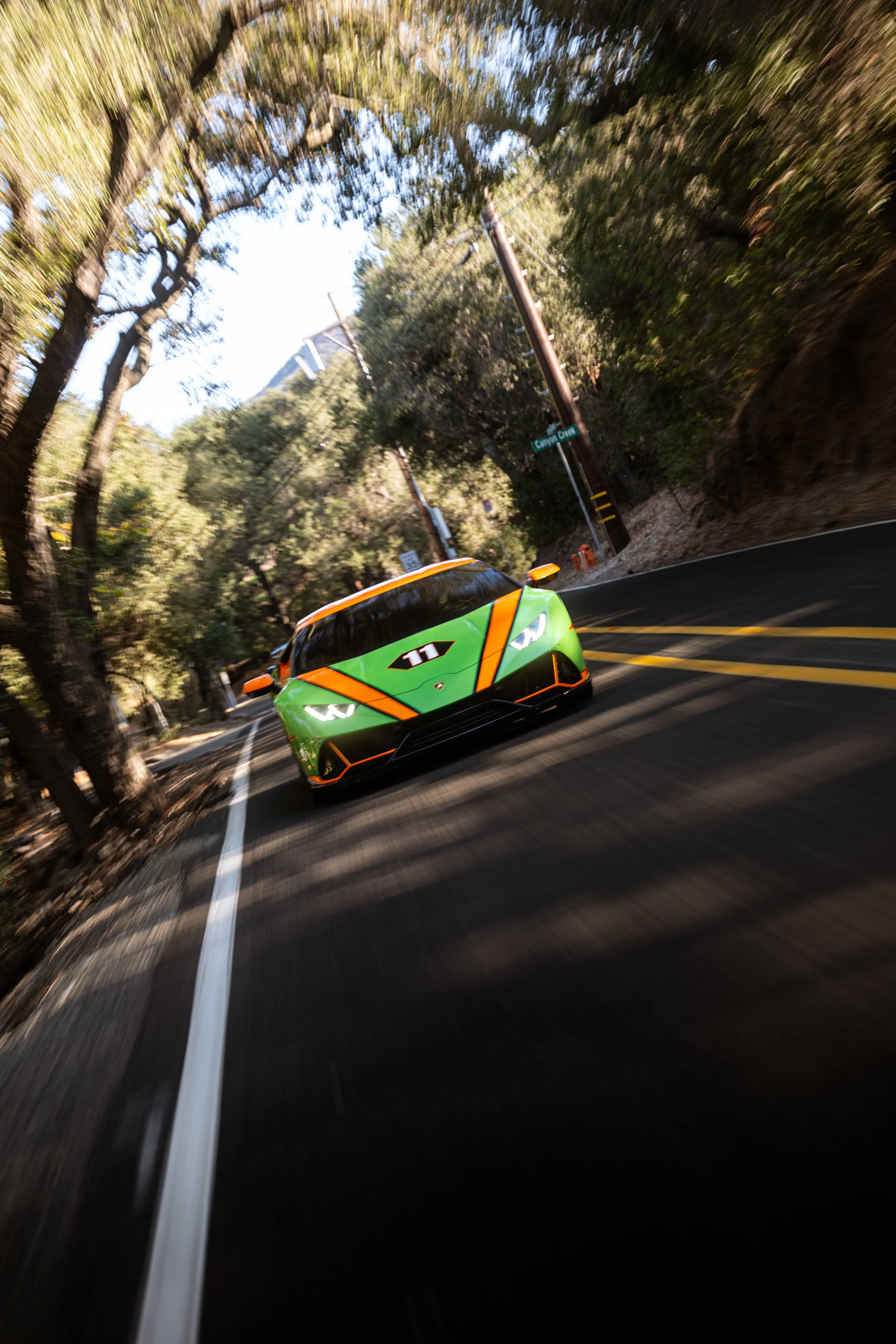 Green and orange Lamborghini race car driving on a forested mountain road near Canyon Drive