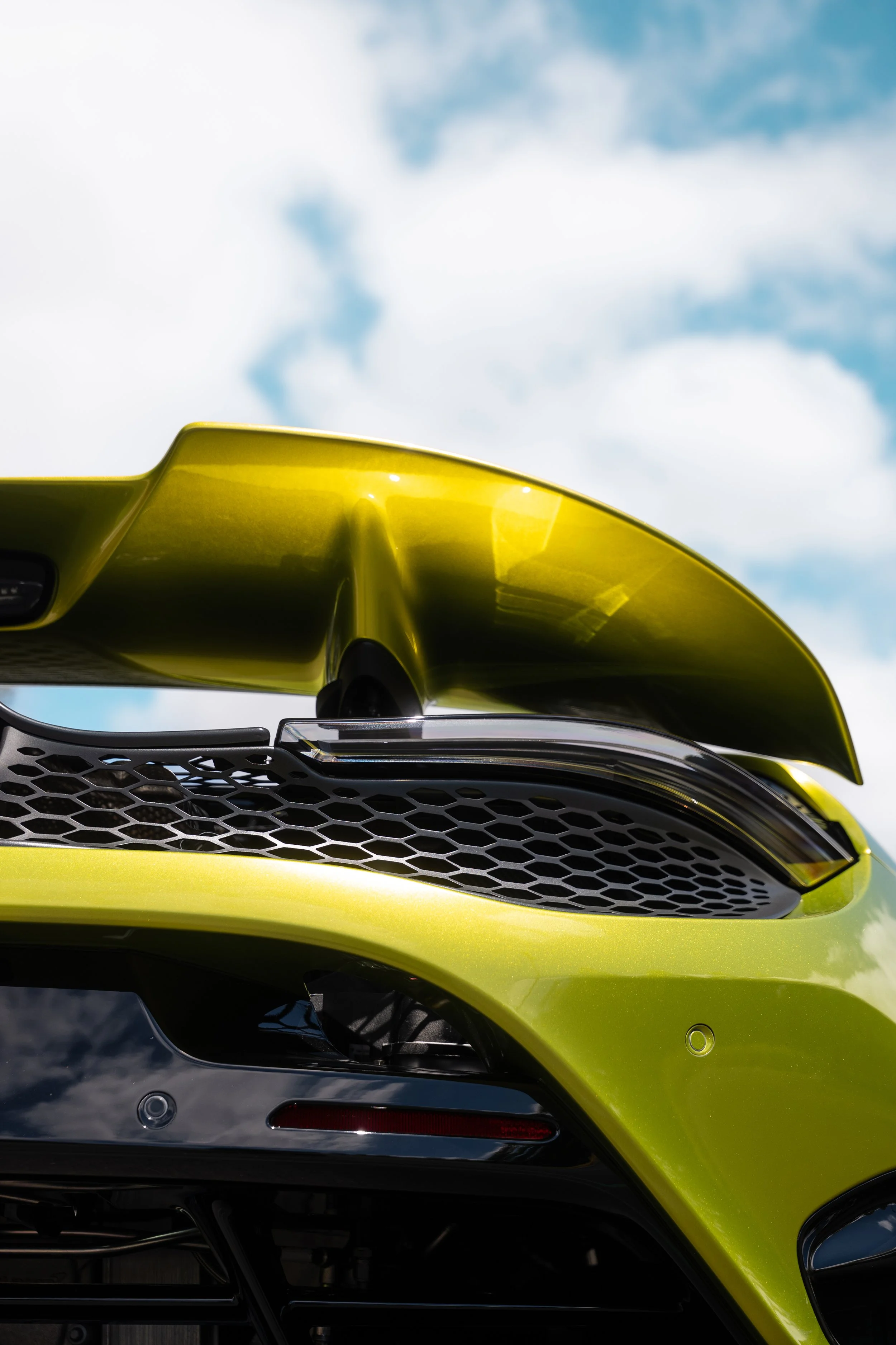 Close-up of a flux green McLaren with a black honeycomb grille and rear spoiler against a blue sky