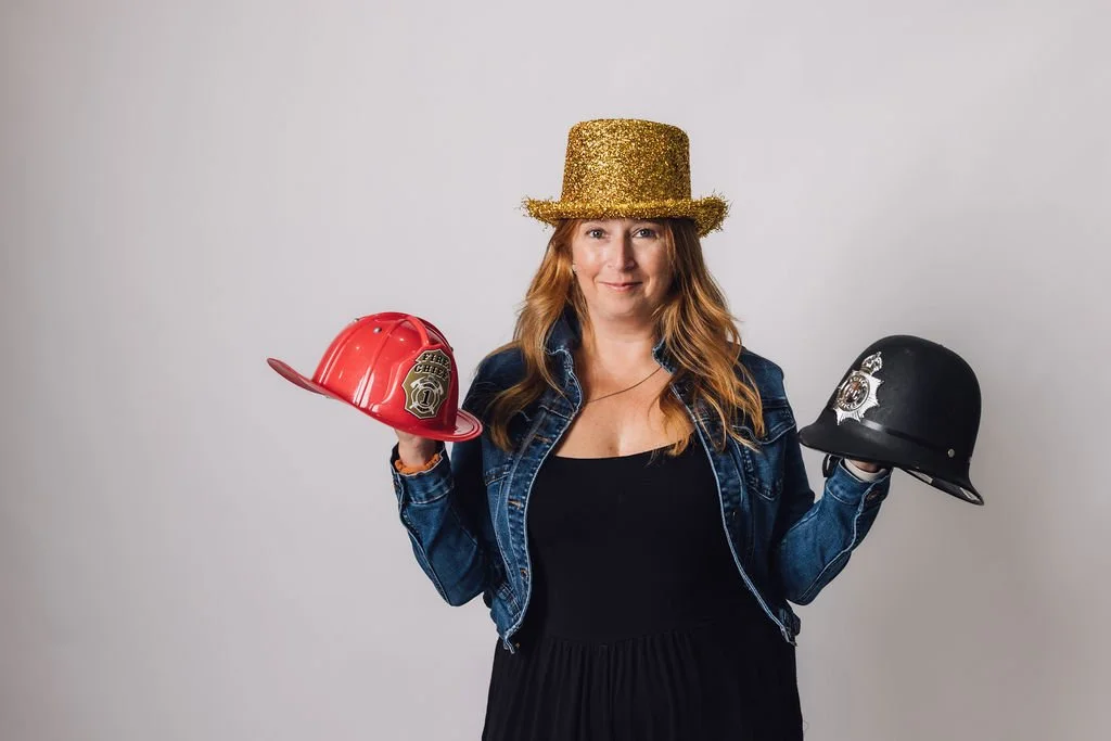Portrait de Julie portant un chapeau haut de forme doré sur la tête et des chapeaux de pompier et police dans les mains.