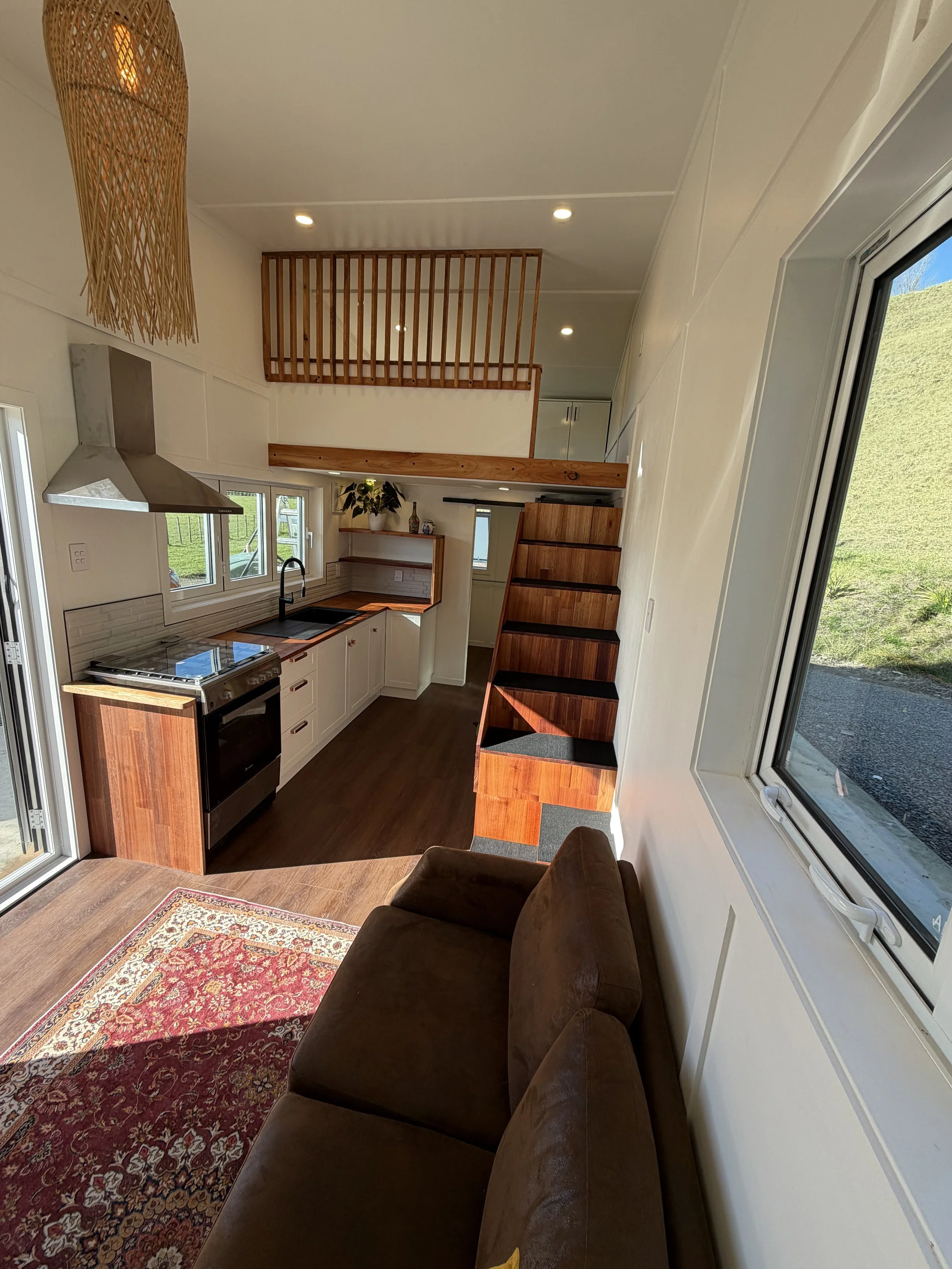 Tiny Timber Homes rental interior with kitchen, timber staircase, loft, and lounge seating