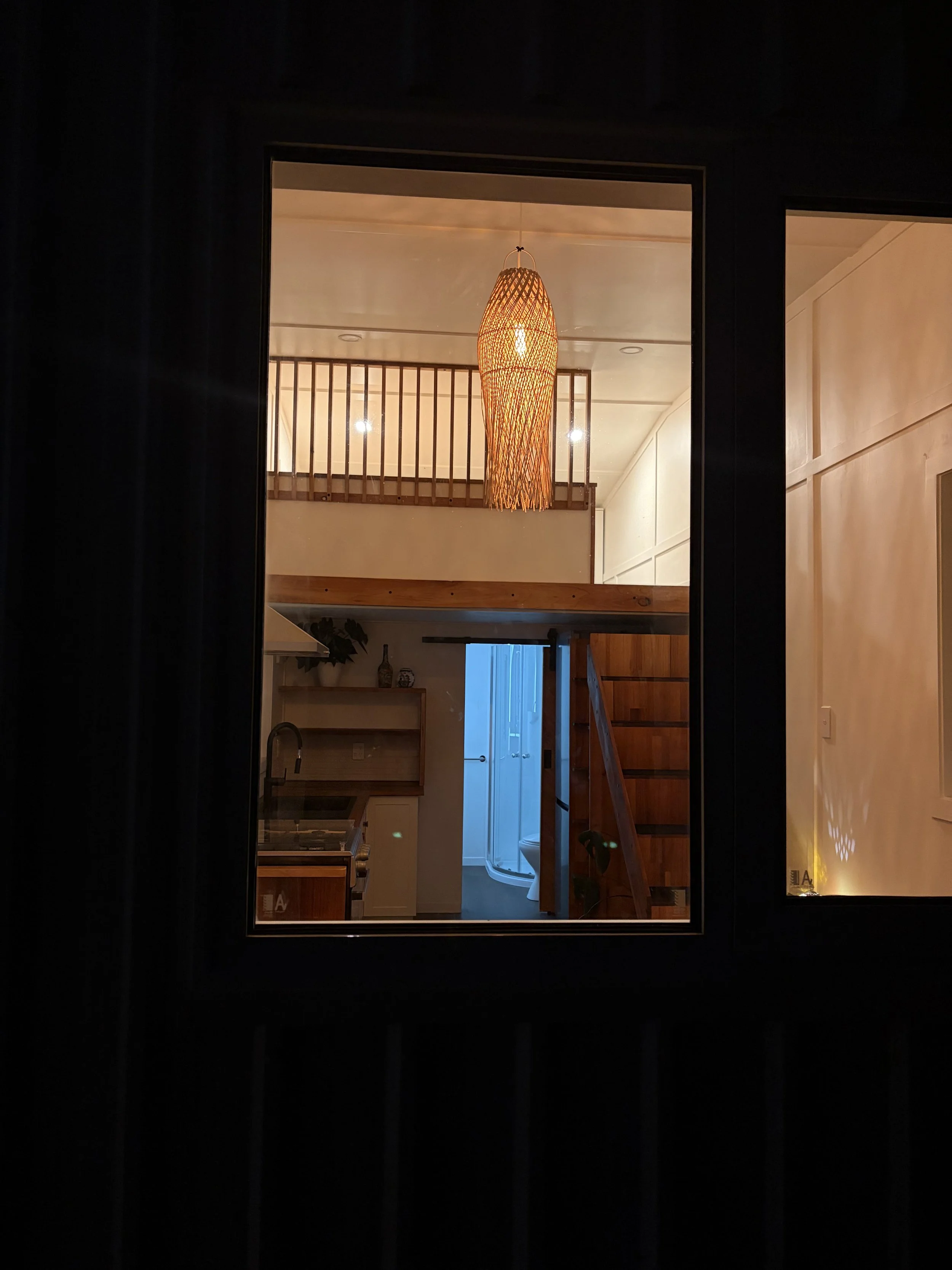 Nighttime view through window into Tiny Timber Homes rental loft, kitchen, and bathroom