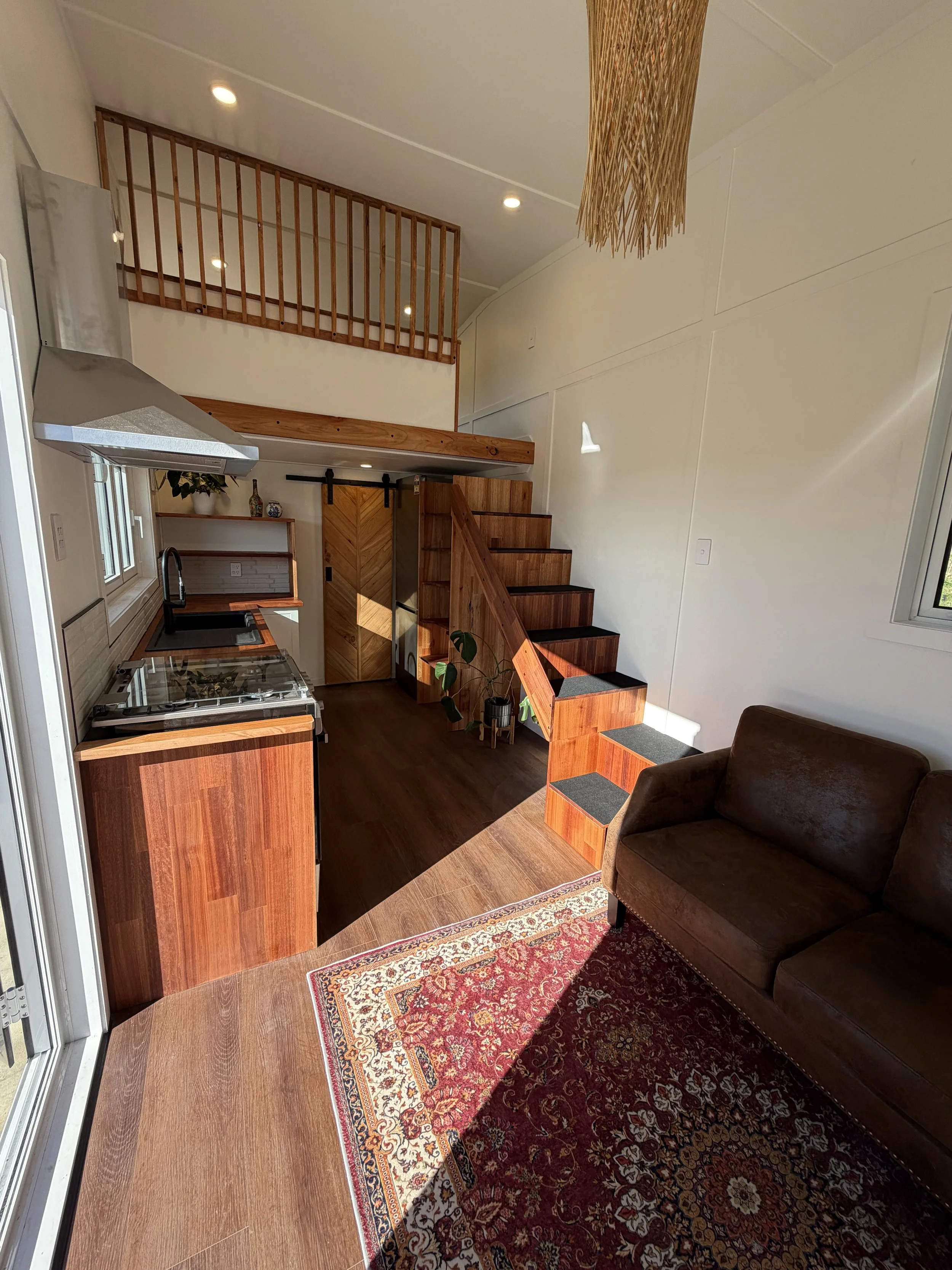 Tiny Timber Homes rental interior showing timber shelving, kitchen, and lounge with Persian rug