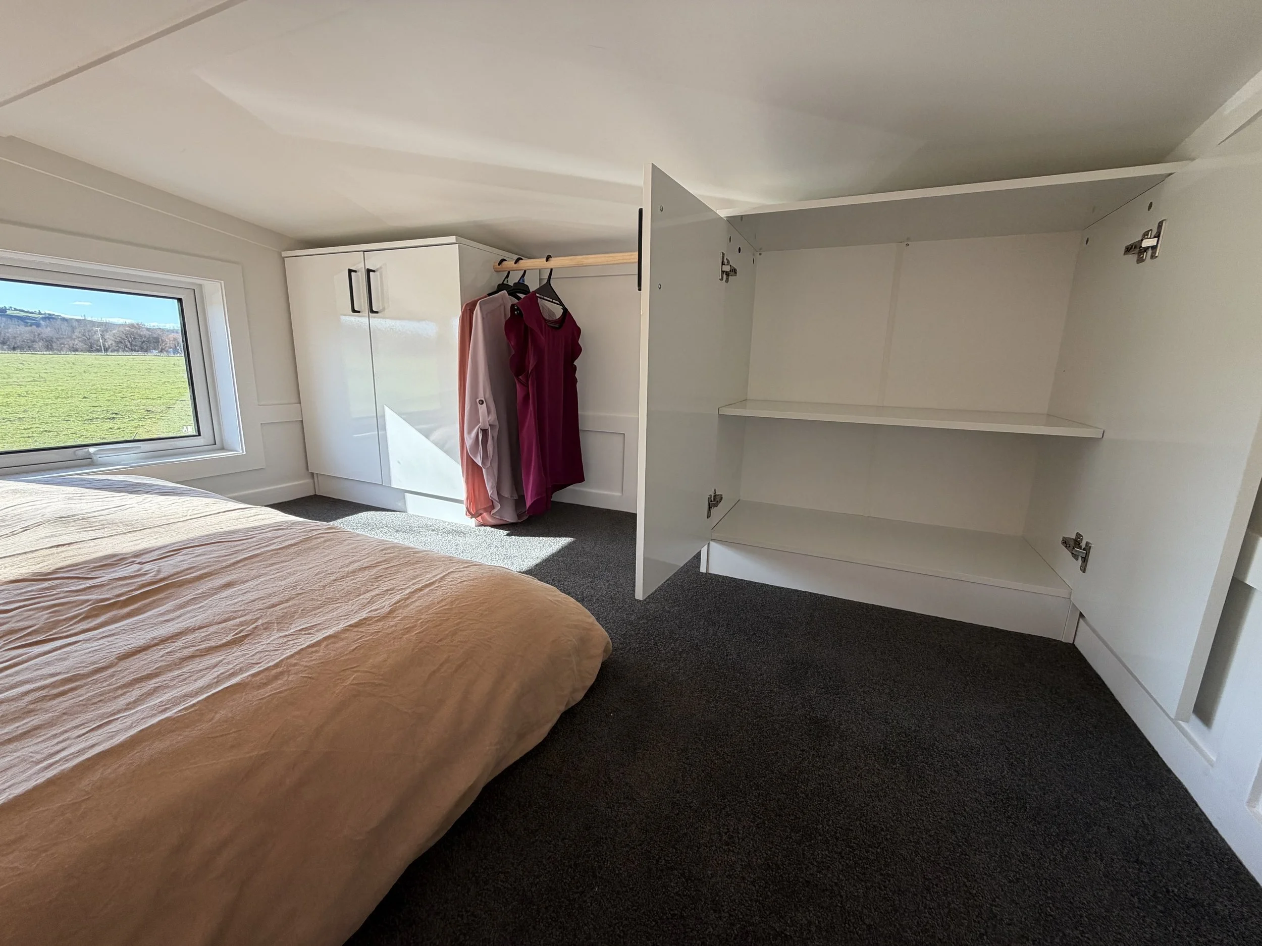 Tiny Timber Homes rental loft bedroom with open wardrobe storage and hanging clothes rail