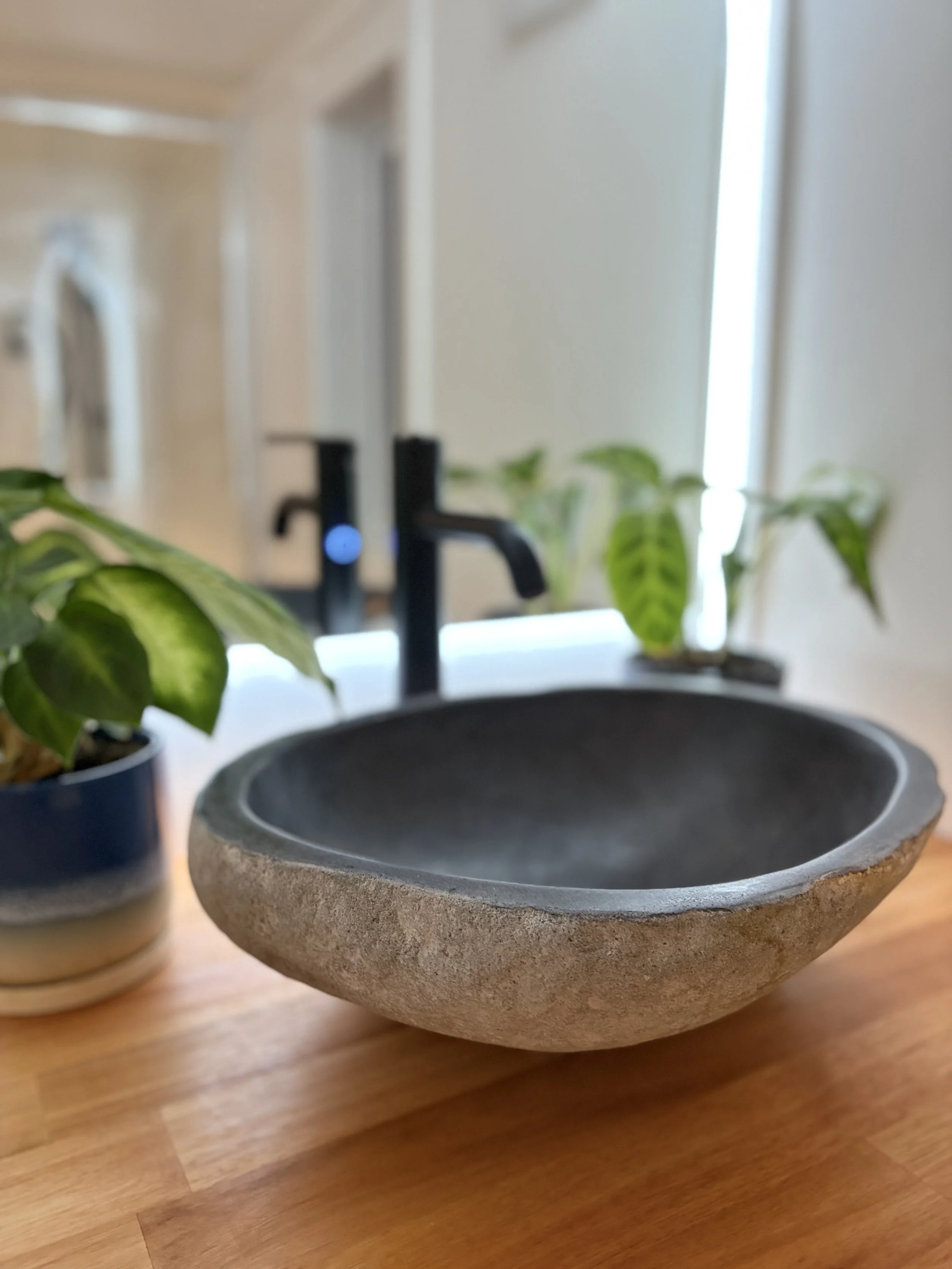 Close-up of stone vessel sink on timber vanity with black tap and potted plants