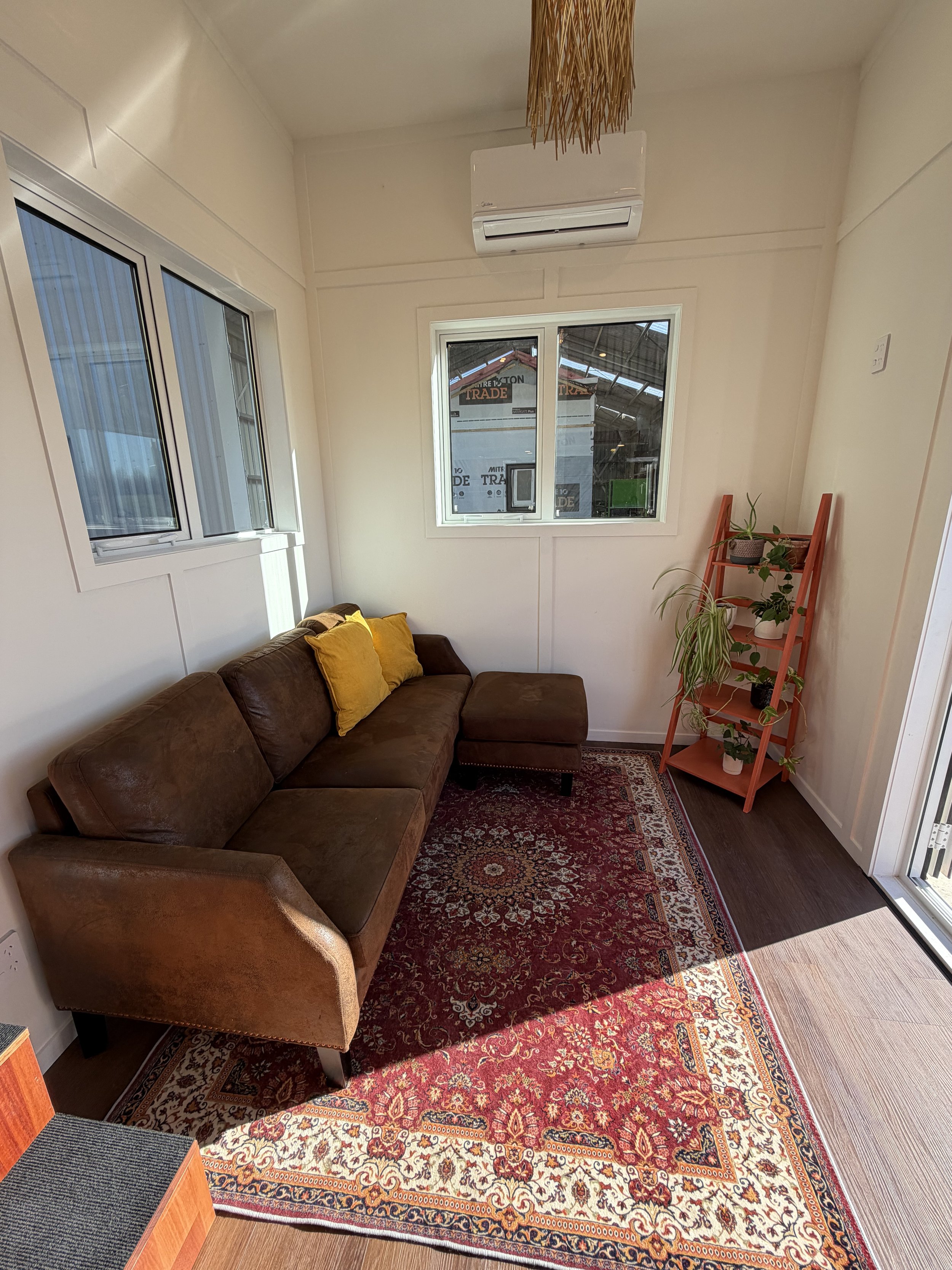 Tiny Timber Homes rental lounge with brown leather sofa, Persian-style rug, heat pump air conditioning, and plant ladder shelf