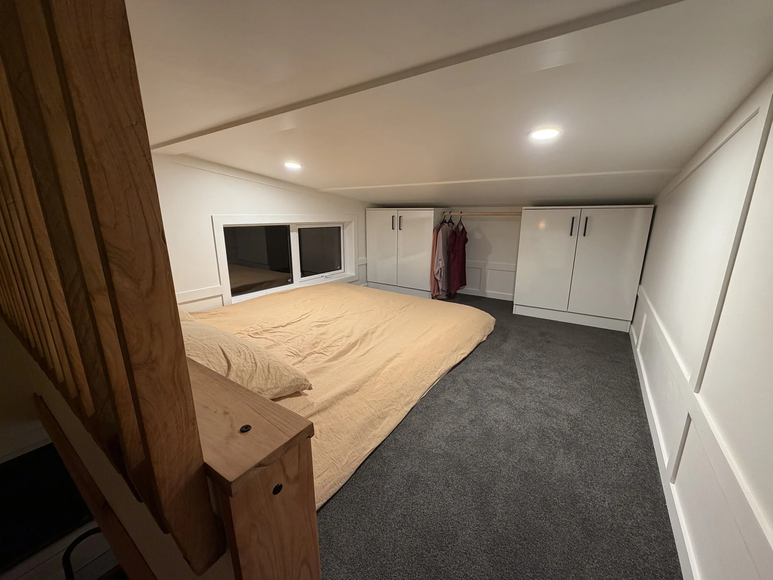 Tiny Timber Homes rentals loft bedroom with double bed, timber staircase, and built-in wardrobe storage with hanging rail