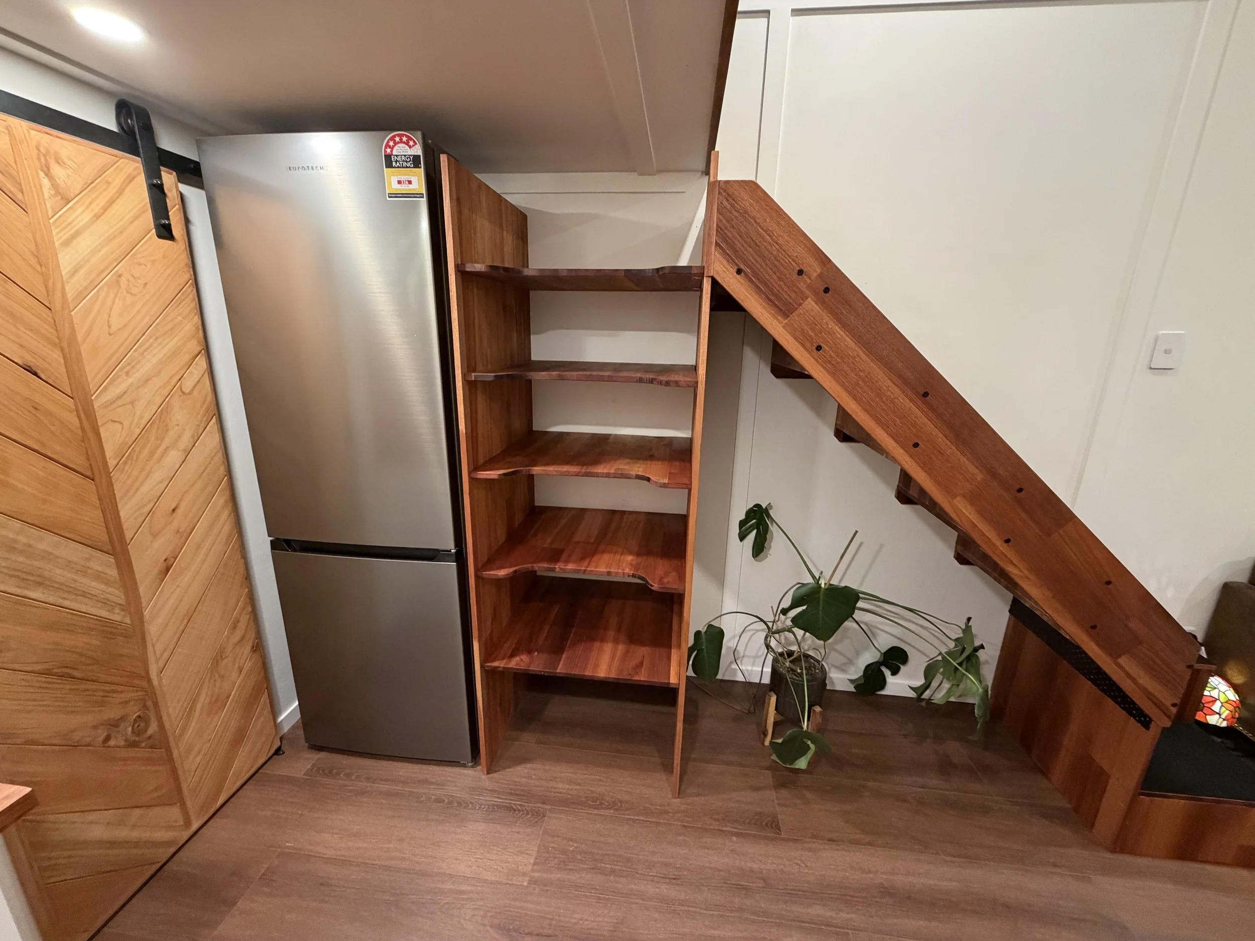 Tiny Timber Homes rental kitchen with fridge, understairs shelving, and chevron barn door