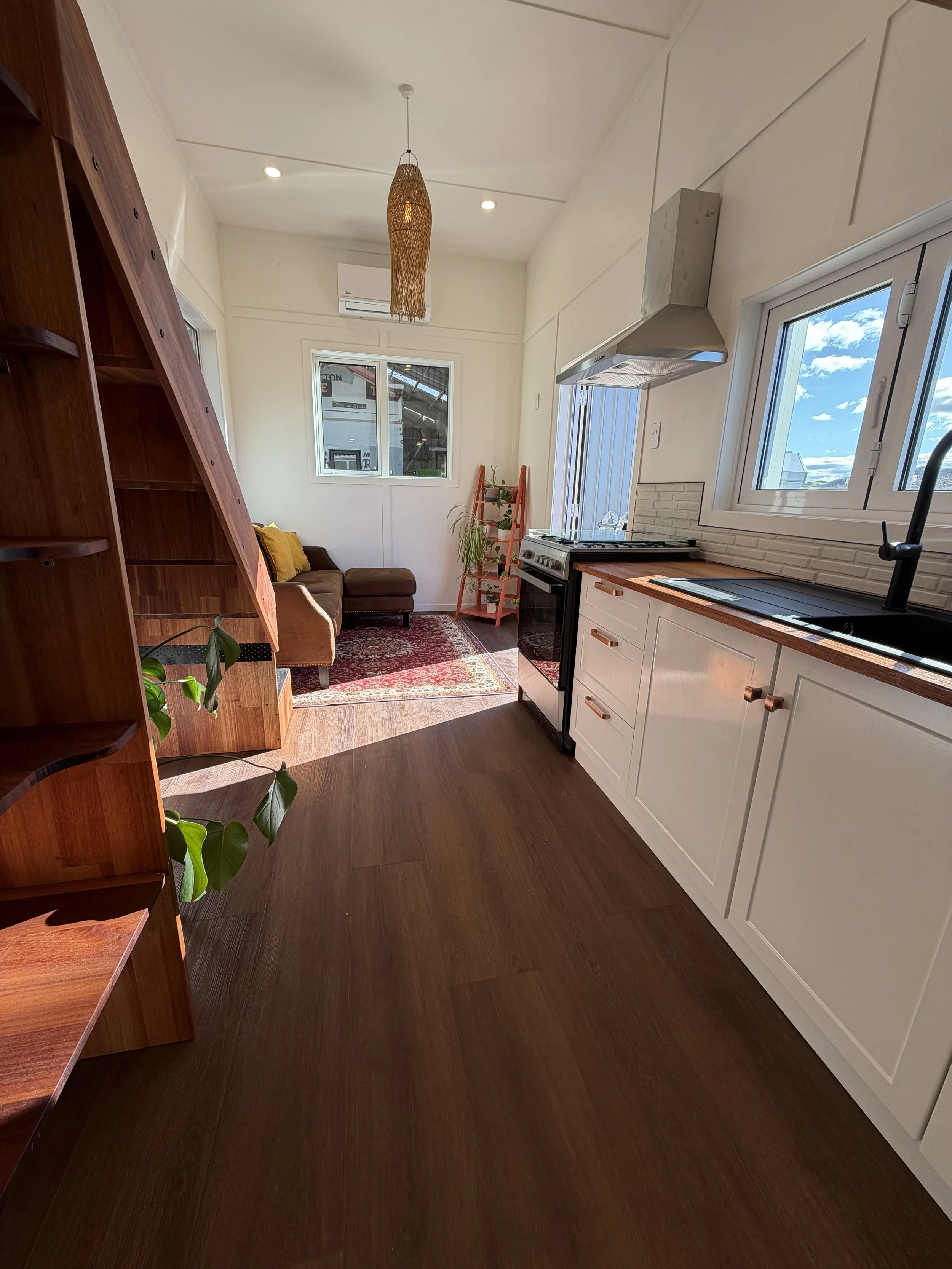 Tiny Timber Homes rental kitchen with timber staircase, loft railing, and countryside window views