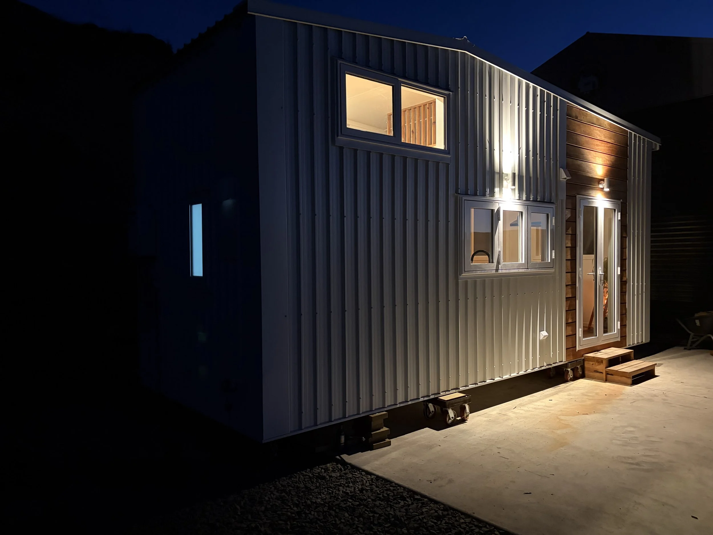 Tiny Timber Homes rental exterior at night with corrugated cladding and glowing windows