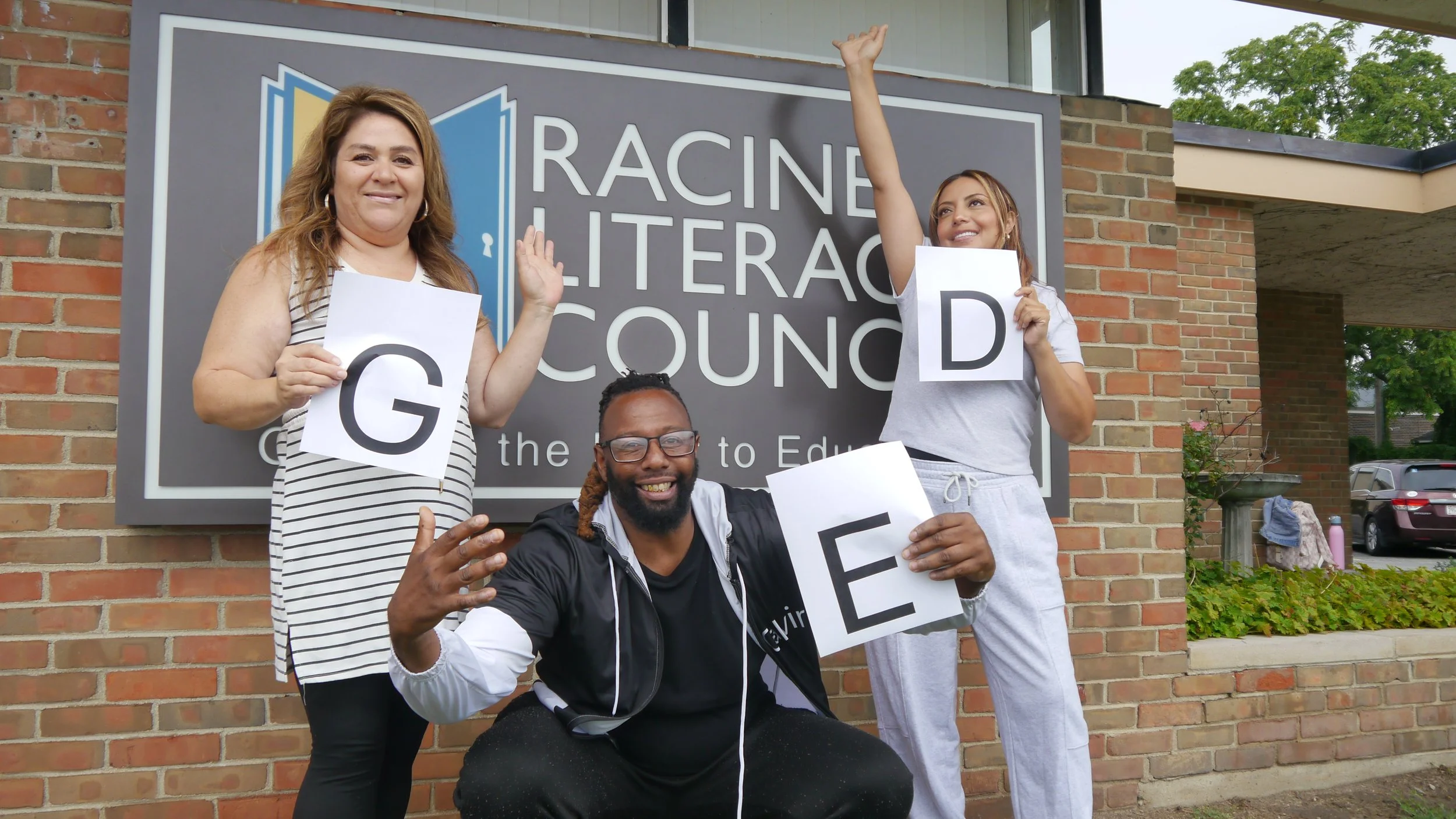 Three GED students standing in front of the Racine Literacy Council building.