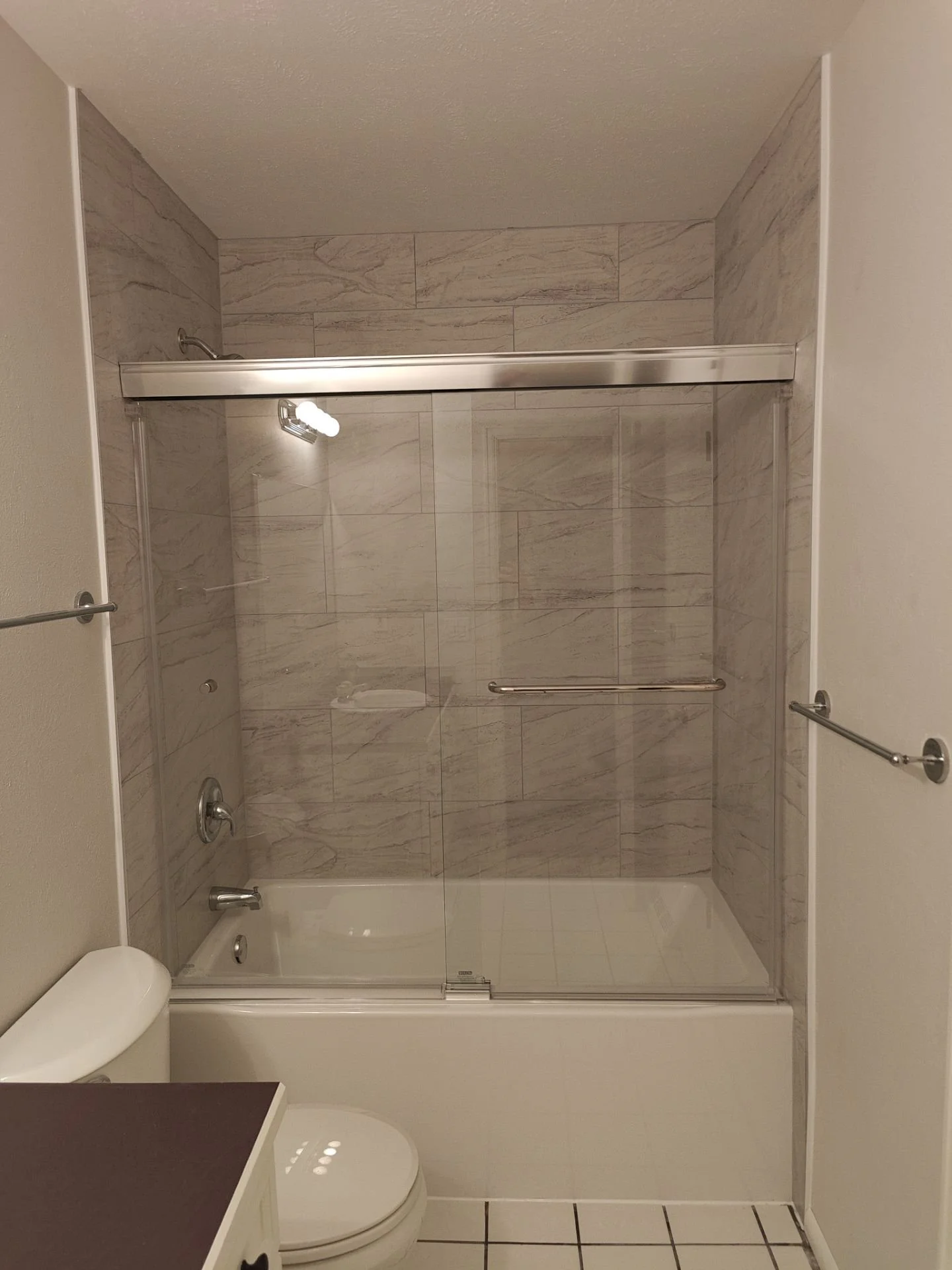Completed Arvada bathtub replacement with gray ceramic tile and Delta Portwood semi-frameless sliding glass shower door.