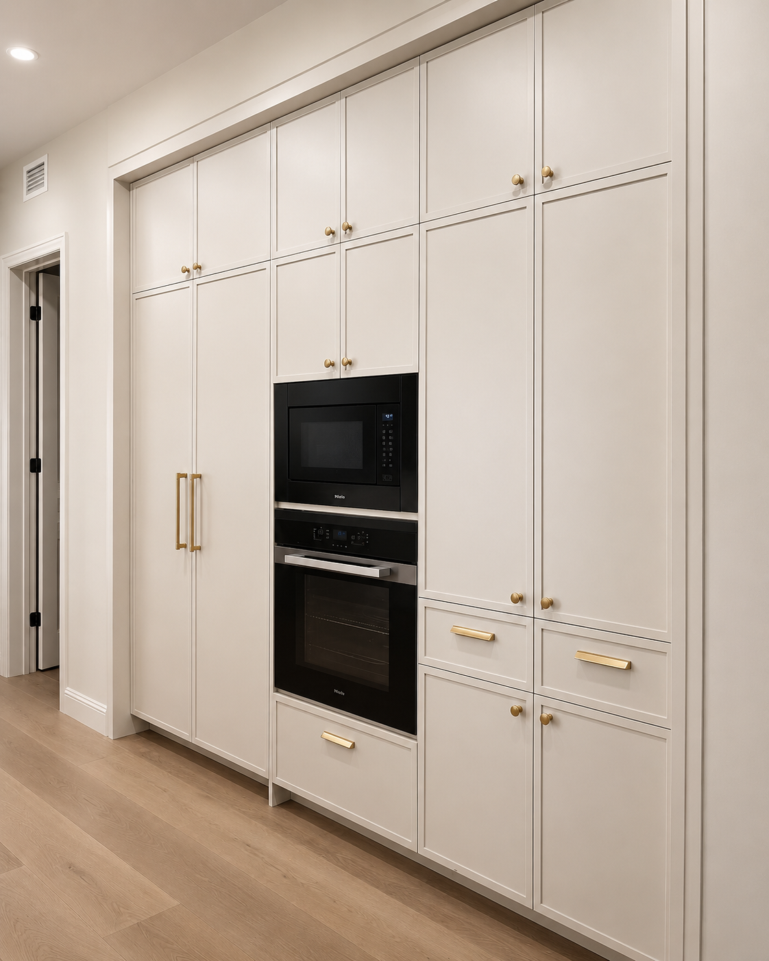 White built-in kitchen cabinets with gold knobs, a black microwave, and oven, with a wood floor.