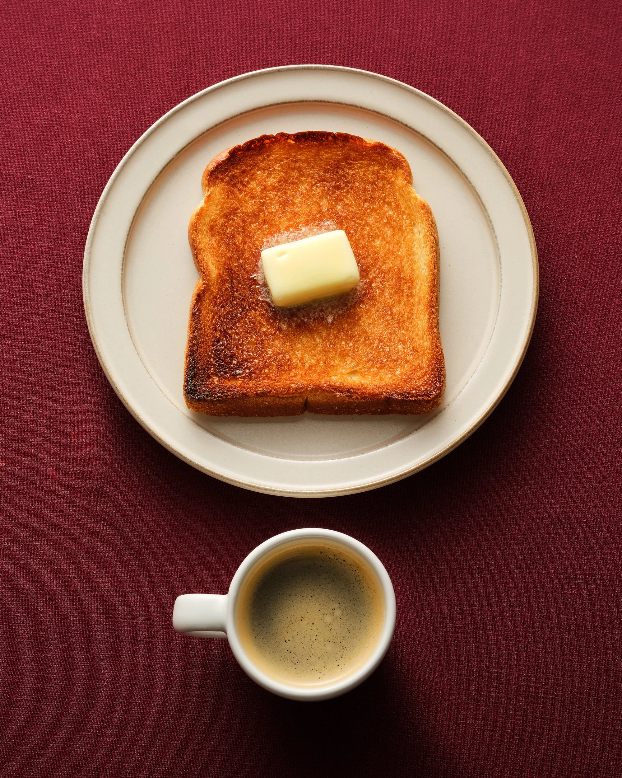 버터가 올라간 구운 식빵과 에스프레소 한 잔. 버건디 컬러 배경의 미니멀한 푸드 스타일링.