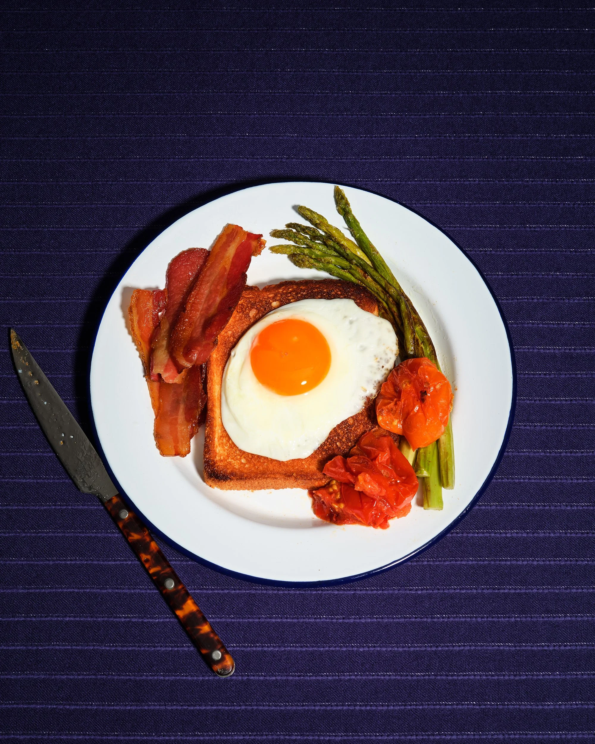 보라색 배경 위 베이컨과 계란후라이 토스트. 과감한 컬러 매치의 상업 사진.