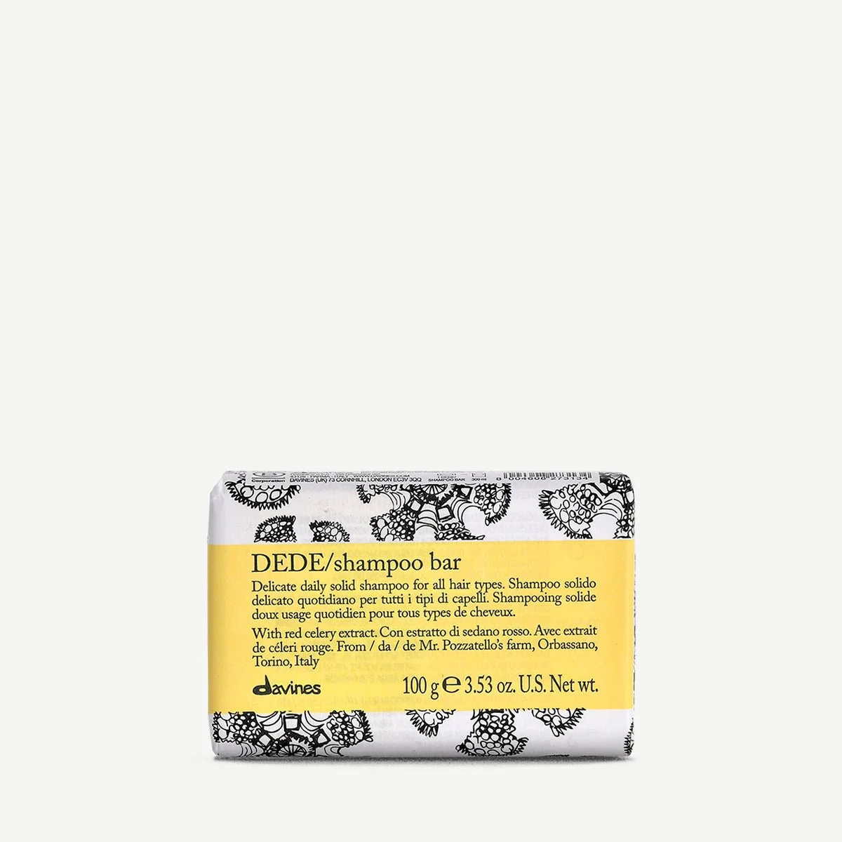Bar of Davines DEDE shampoo with yellow label, black floral pattern, and text describing it as a solid shampoo with red celery extract, weighing 100 grams.