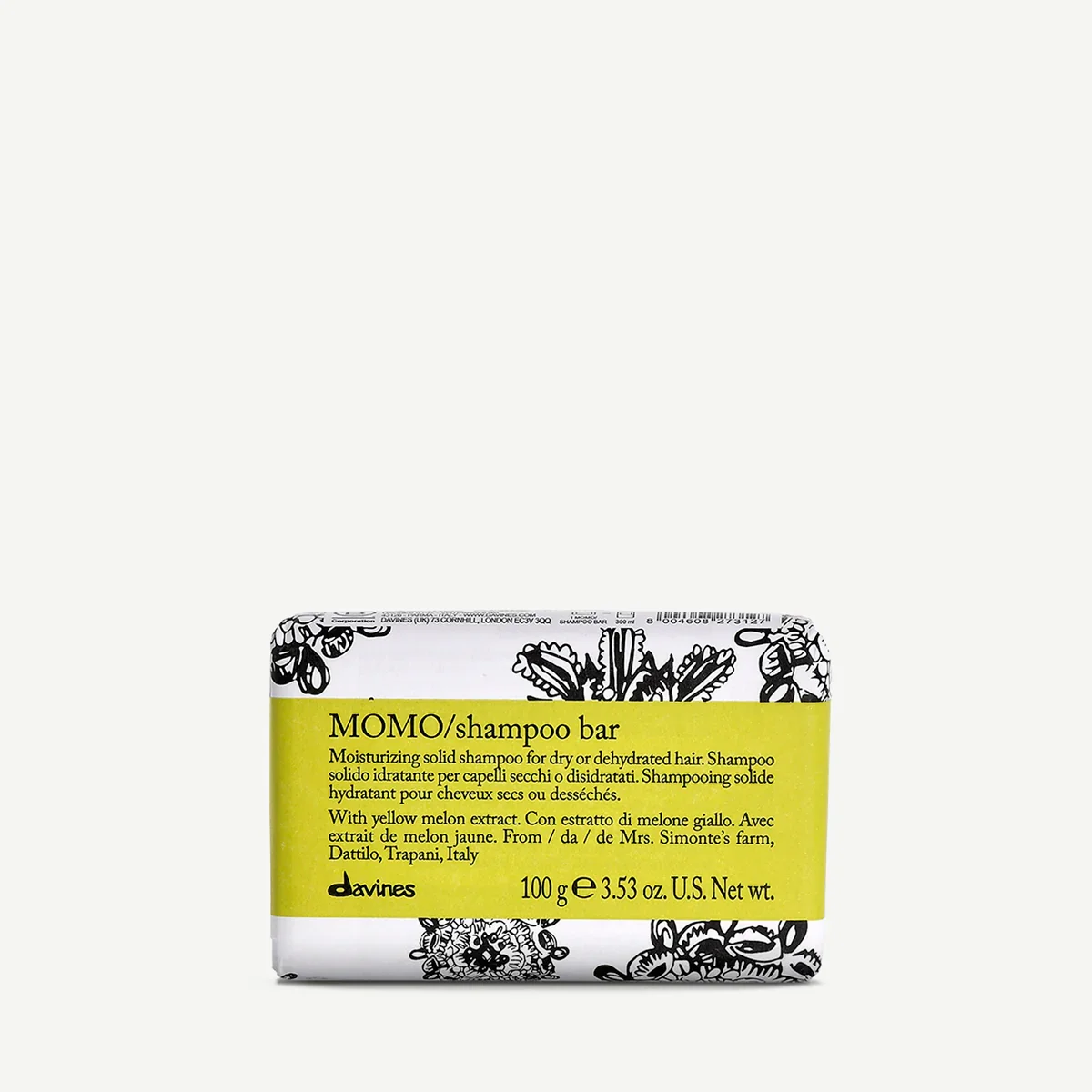 A bar of MOMO shampoo with a black and white floral pattern on the packaging and a yellow label indicating it contains yellow melon extract. The text on the label describes it as a moisturizing solid shampoo for dry or dehydrated hair, weighing 100 g