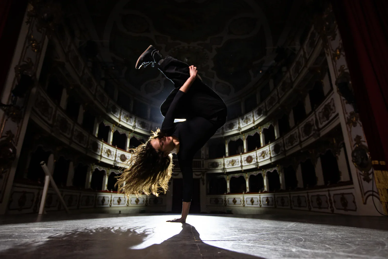 A dancer performing a handstand on stage in an ornate theater.