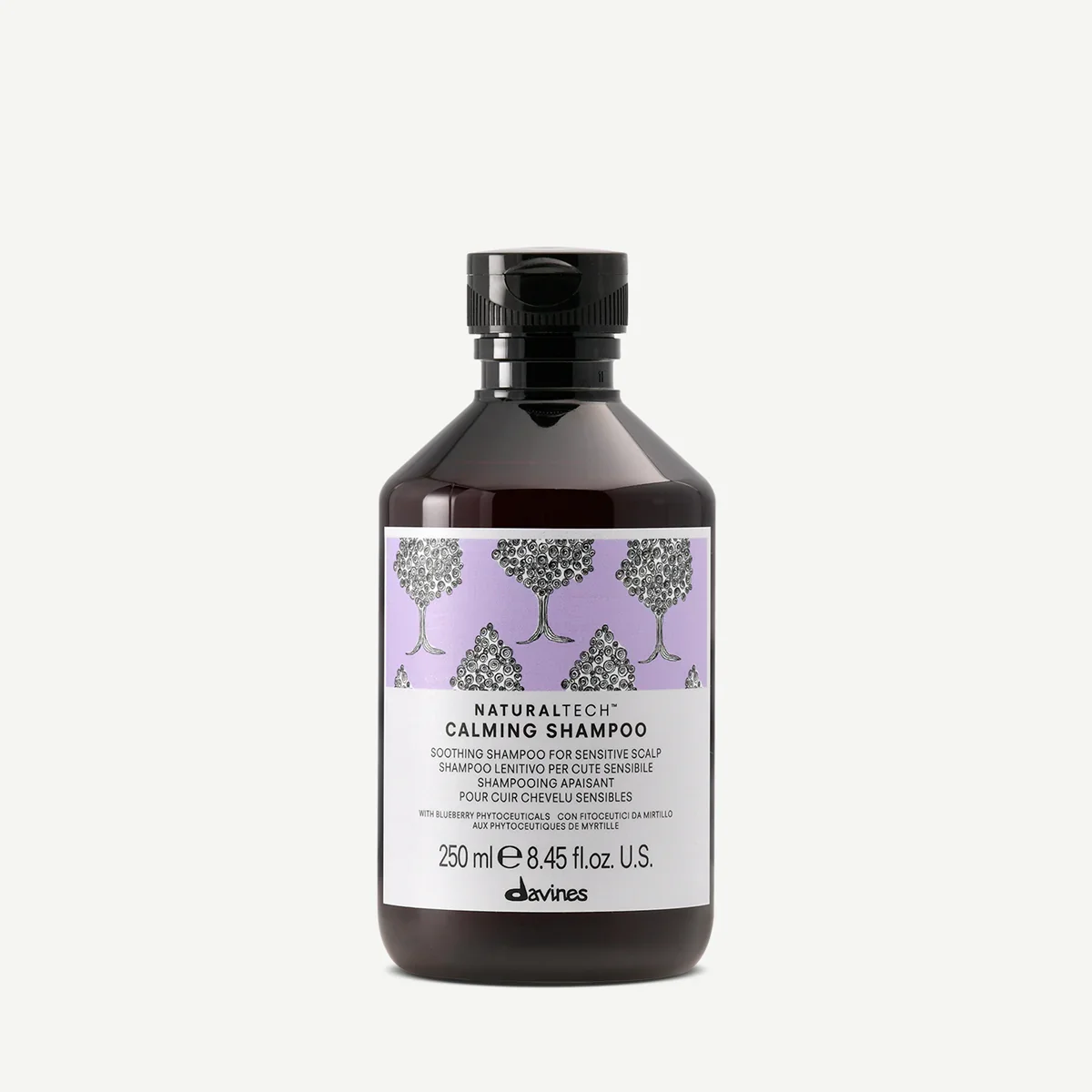A bottle of Davines Natural Tech Calming Shampoo with a purple and gray label featuring illustrations of trees.