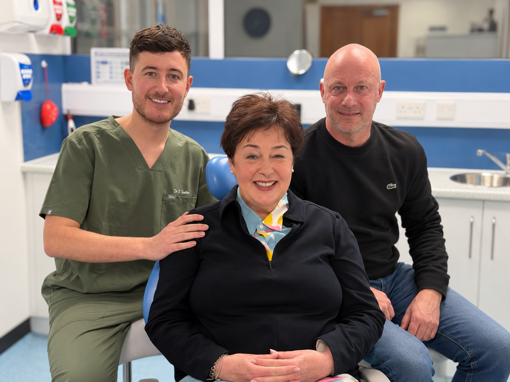 Dr Alister Seaton in green scrubs, smiling with two people in a dental surgery.