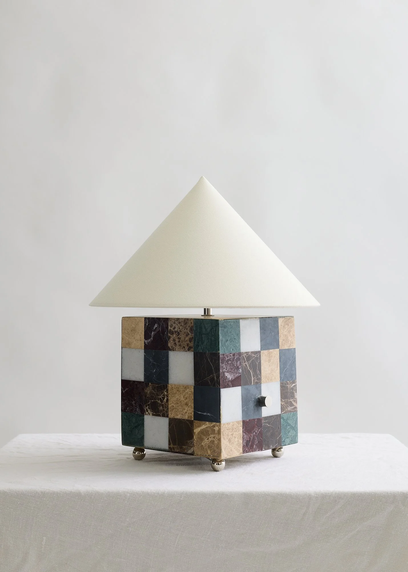 Front view of The Crews table lamp showing its multicolored marble base, rotary dimmer, and ivory fabric shade.