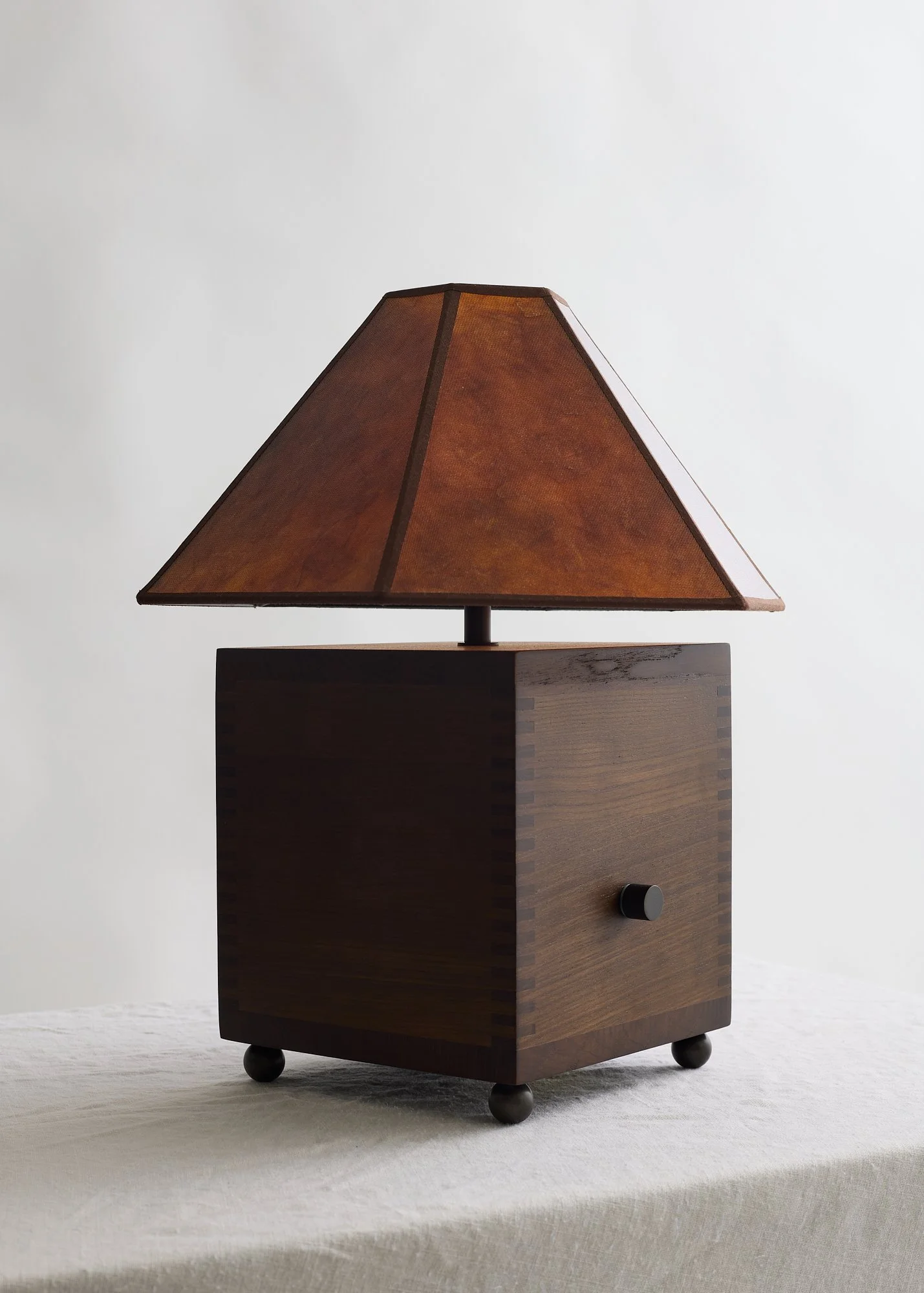 Angled view of The Carley table lamp showing its square walnut base, bronze ball feet, and tapered mica shade.