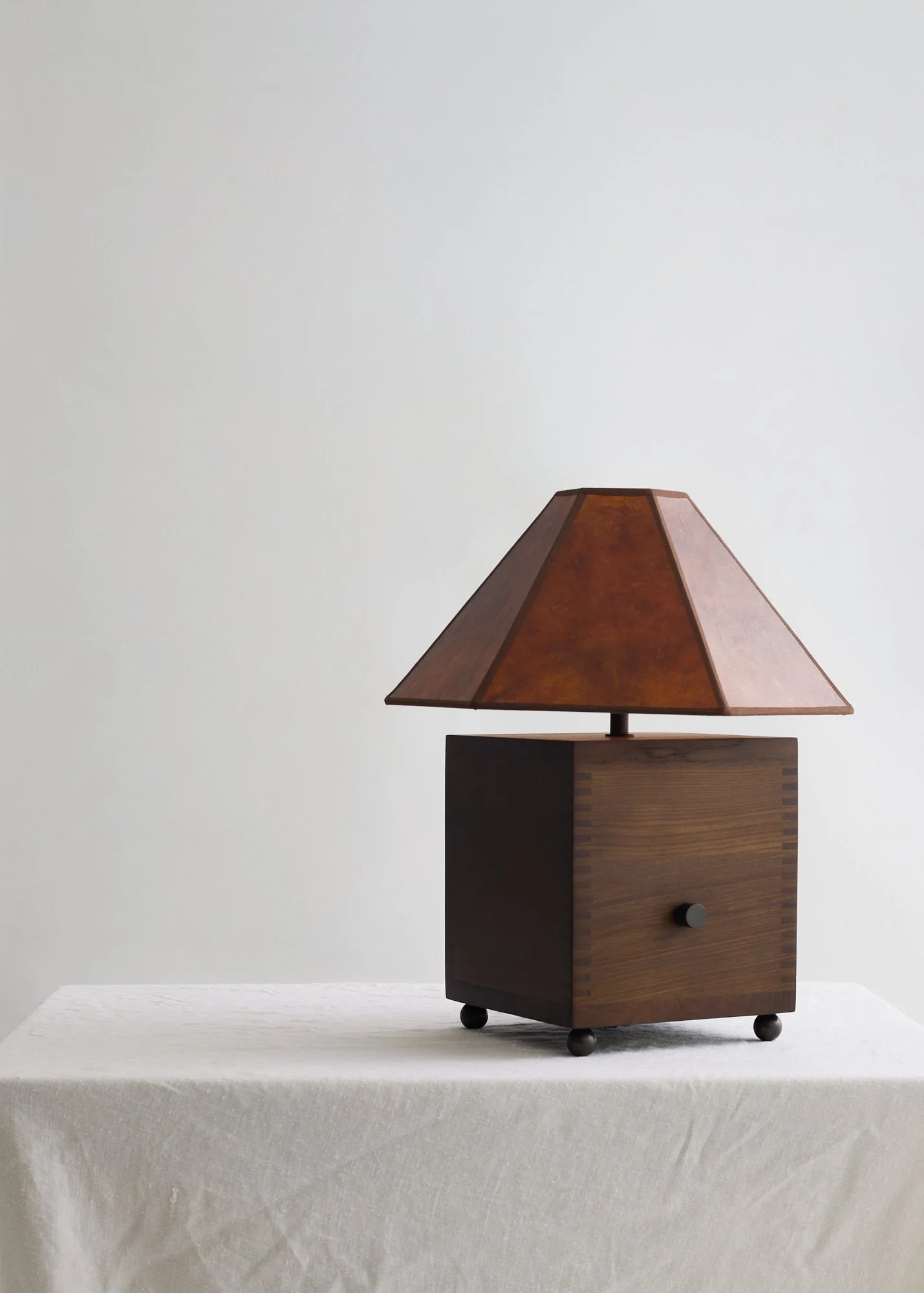 The Carley walnut and mica table lamp viewed at an angle on a pale stone surface against a light wall.