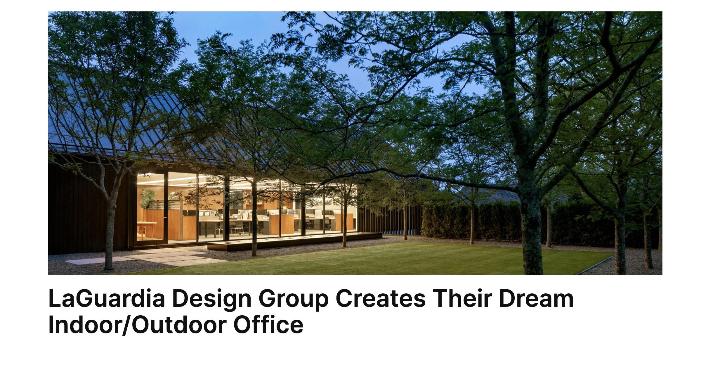 Modern office building with large glass windows, illuminated interior, surrounded by trees and a well-maintained lawn at dusk.