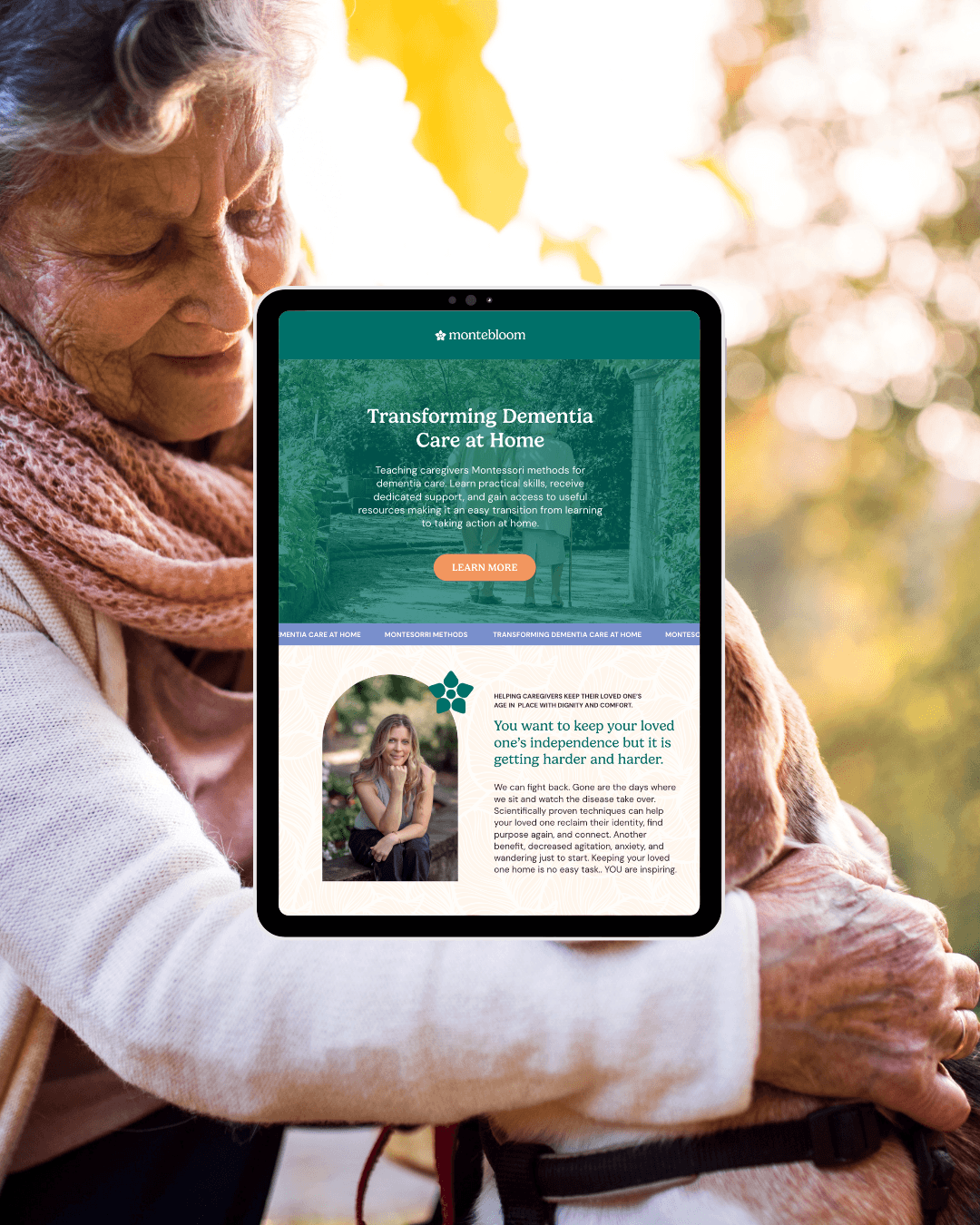 Older woman holding a tablet displaying a website about transforming dementia care at home, with trees and sunlight in the background.