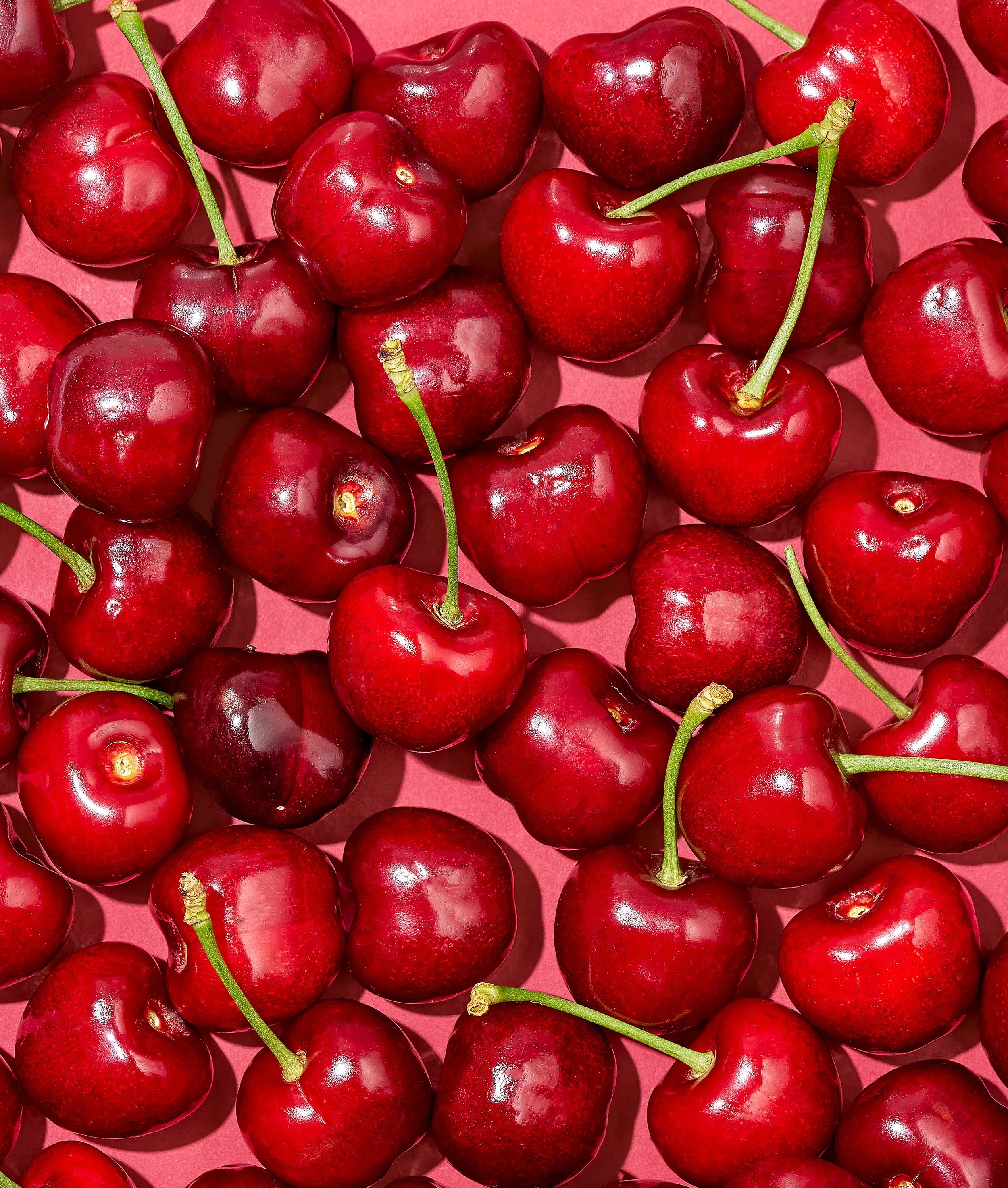 Overhead macro shot of dark red cherries piled densely on a coral pink backdrop for Suzanne Clements' Publix summer produce campaign.