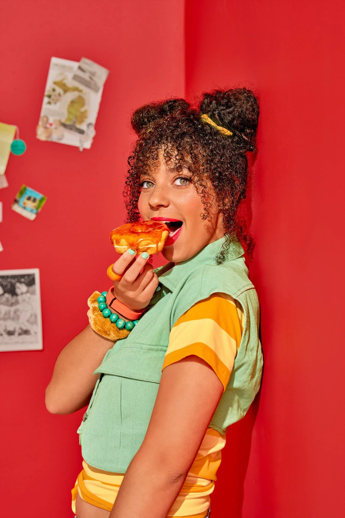 Commercial food lifestyle photography by Suzanne Clements, The Sauce Boss spec campaign: the Sauce Boss character takes a big bite of a hot honey donut, glancing at camera over her shoulder as she leans into a red corner.