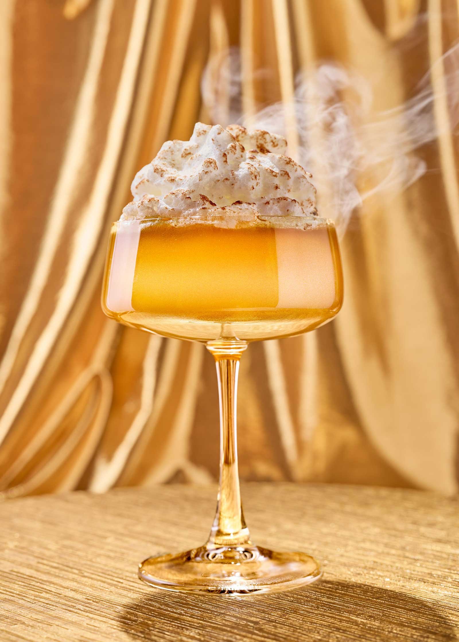 Beverage photograph of a gold bourbon cocktail with a toasted creamy top.