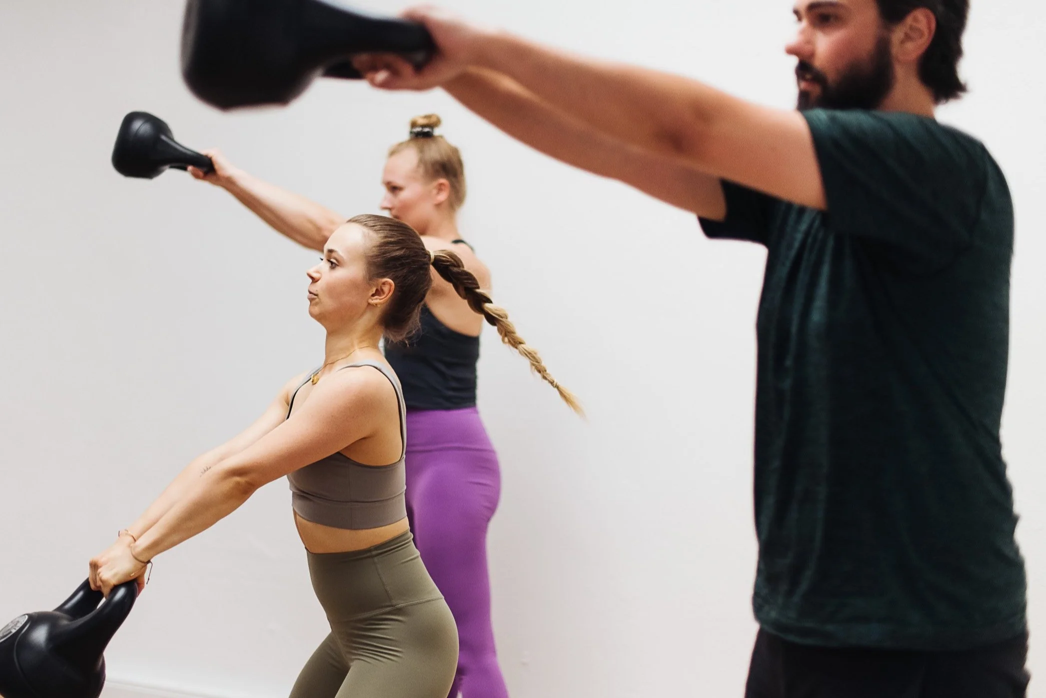 Drei Menschen beim Fitness-Training, die in der Seitenansicht Kraftübungen mit Kettlebells machen.