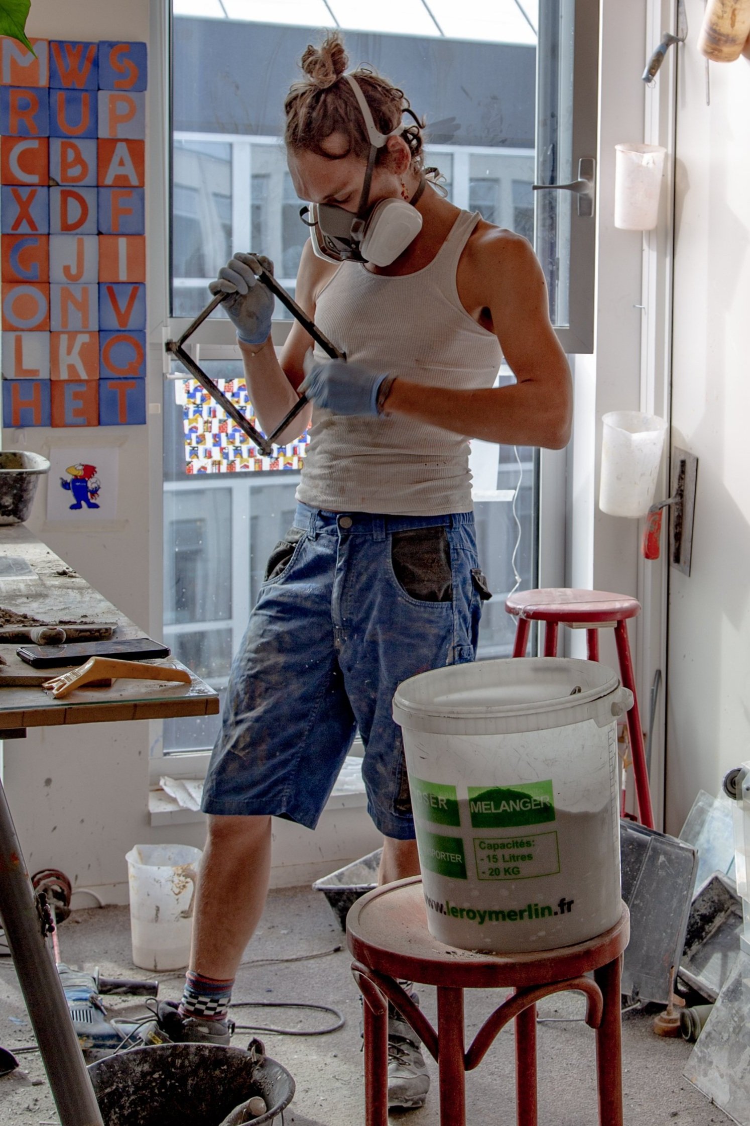 César Bazaar, dans son atelier, fabrique des carreaux de ciments. Il a un masque a gaz sur le visage.