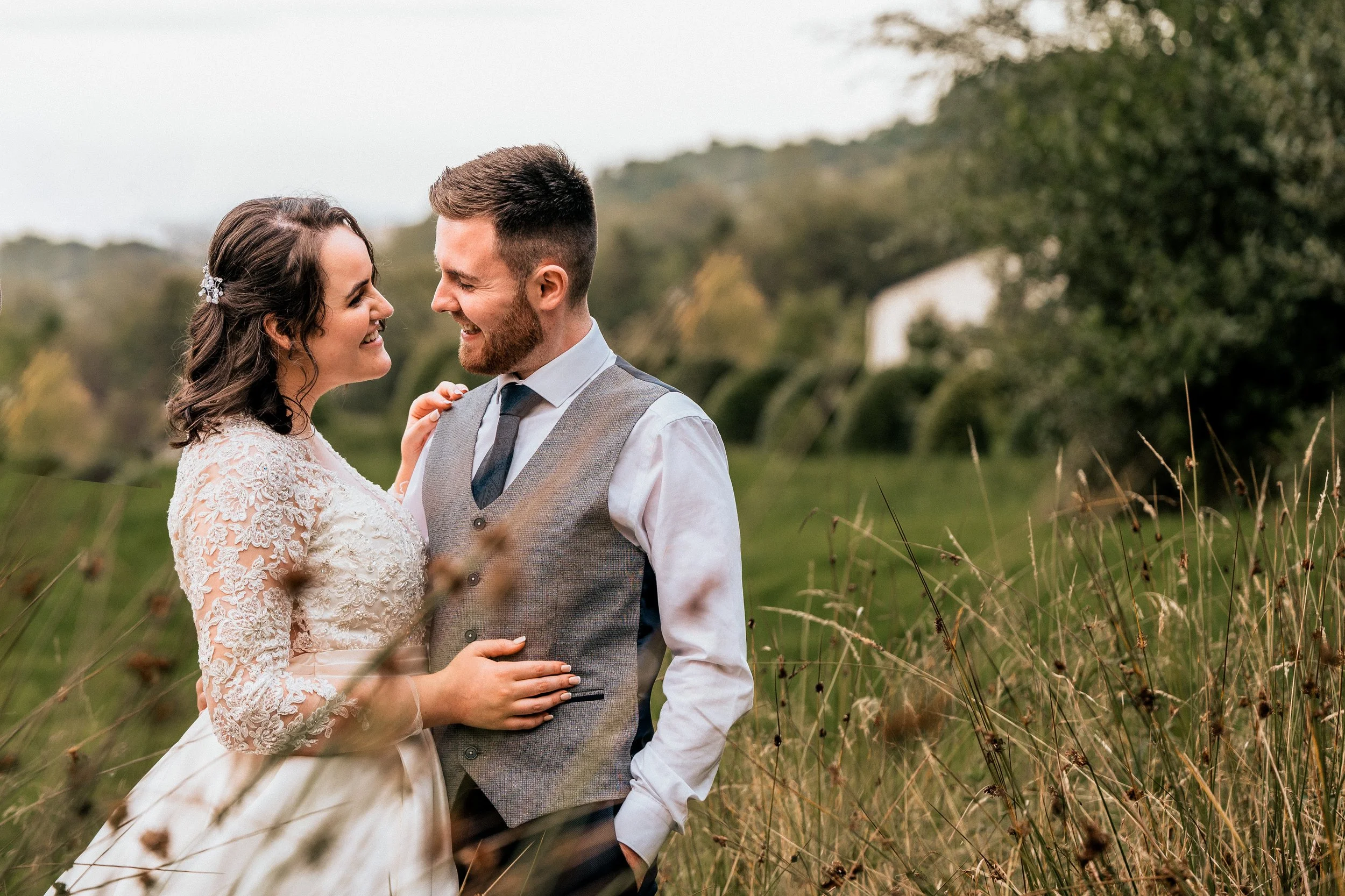 Bride and groom smiling at each other in a field