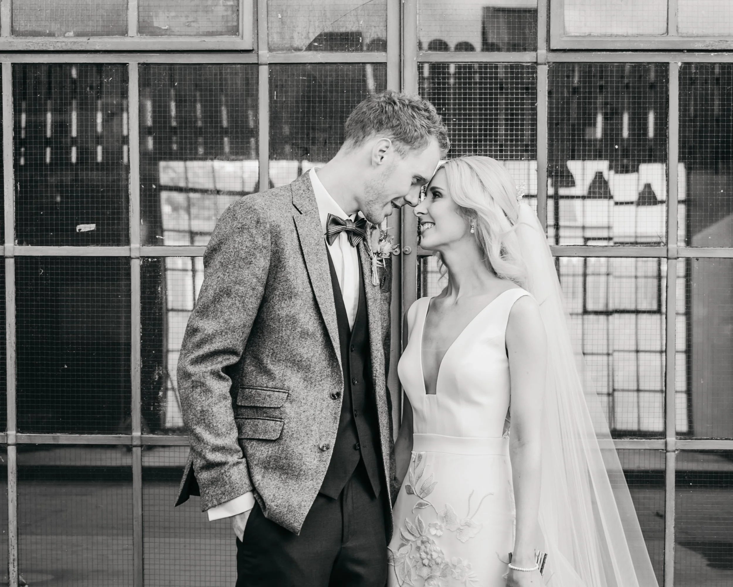 Bride and groom smiling at each other in front of a window.
