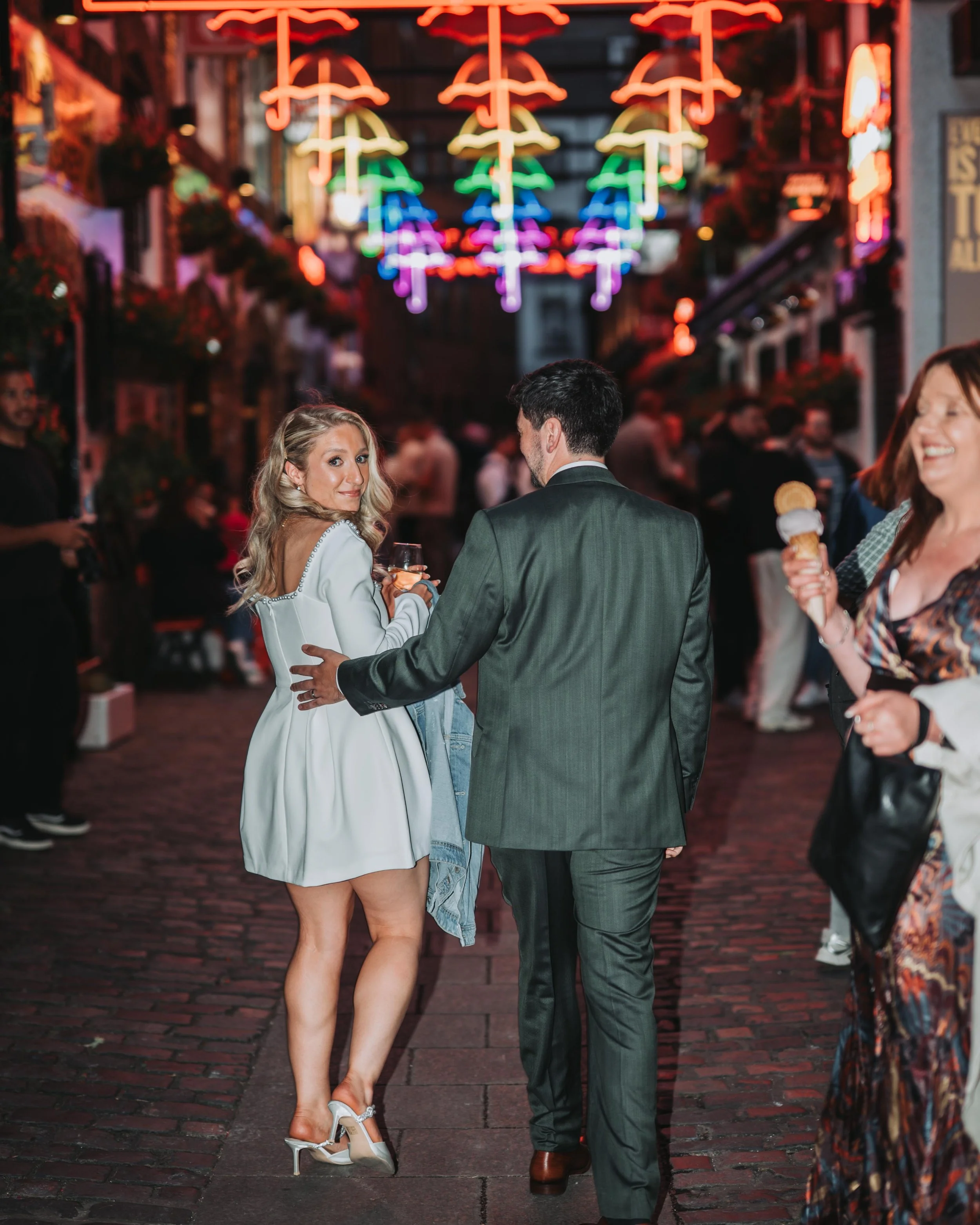 Group of people enjoying nightlife on a cobblestone street decorated with neon umbrella lights