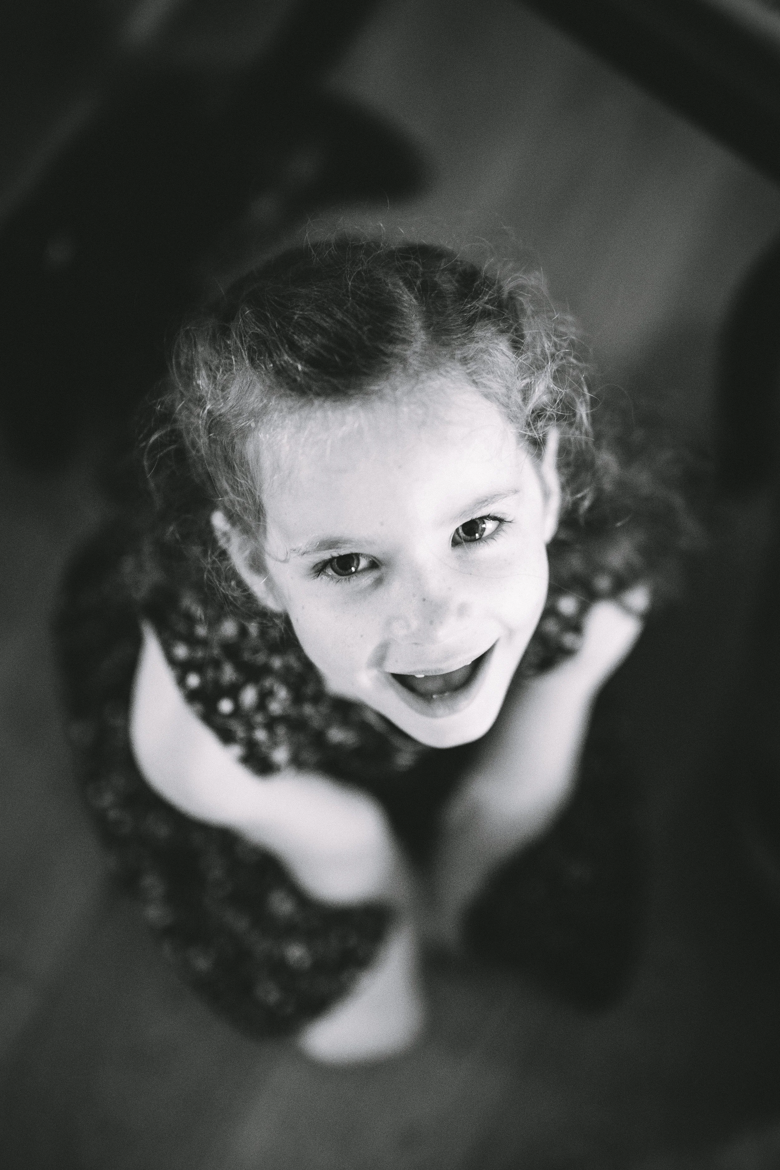 A young girl with curly hair looking up at the camera with an excited expression, smiling widely.