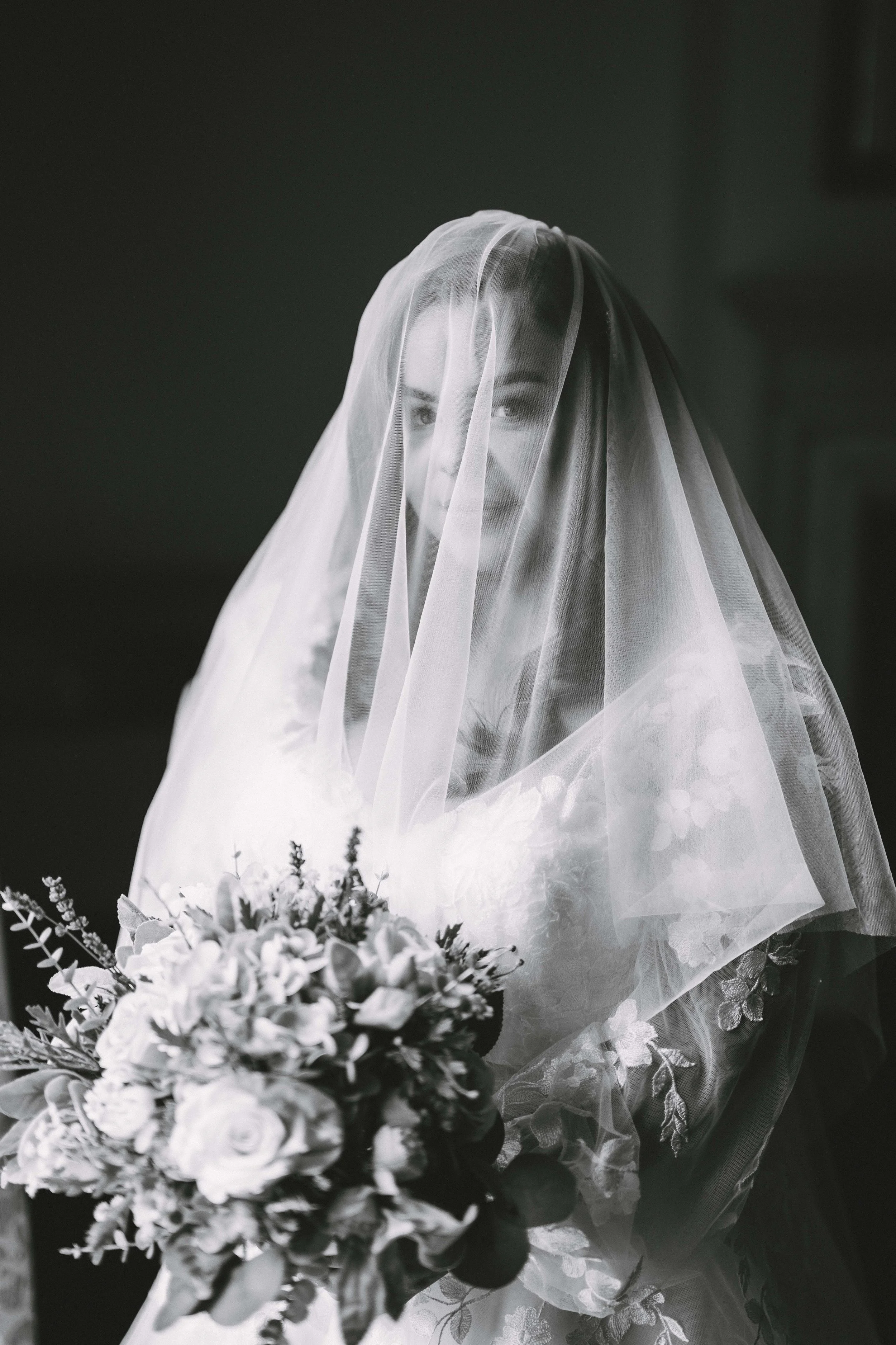 Black and white photo of a woman wearing a bridal veil, holding a bouquet of flowers.