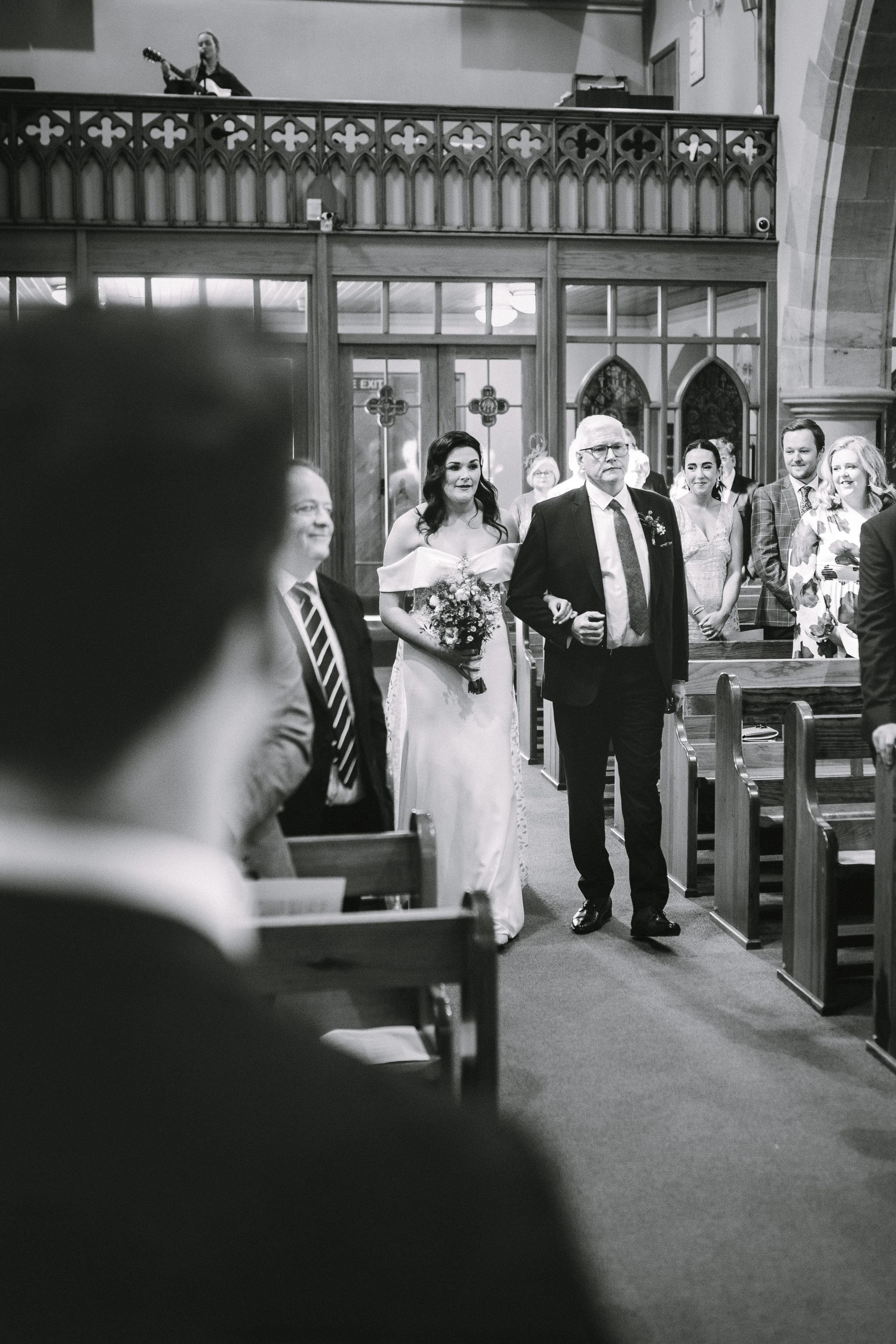 A bride walking down the aisle in a church with her father, surrounded by wedding guests.