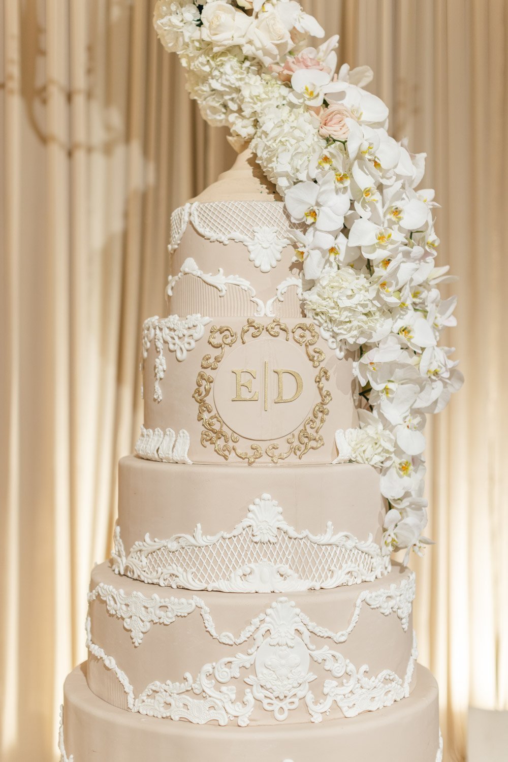 Pale pink and cream roses with white orchids drape a five layer stunning wedding cake with lace and gold accents at the Ritz-Carlton Laguna Niguel