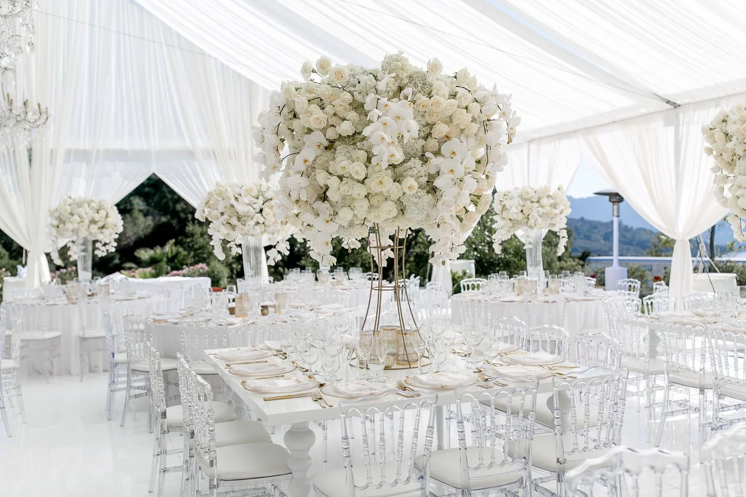 Tented wedding reception with tall white floral centerpiece and clear ghost chairs