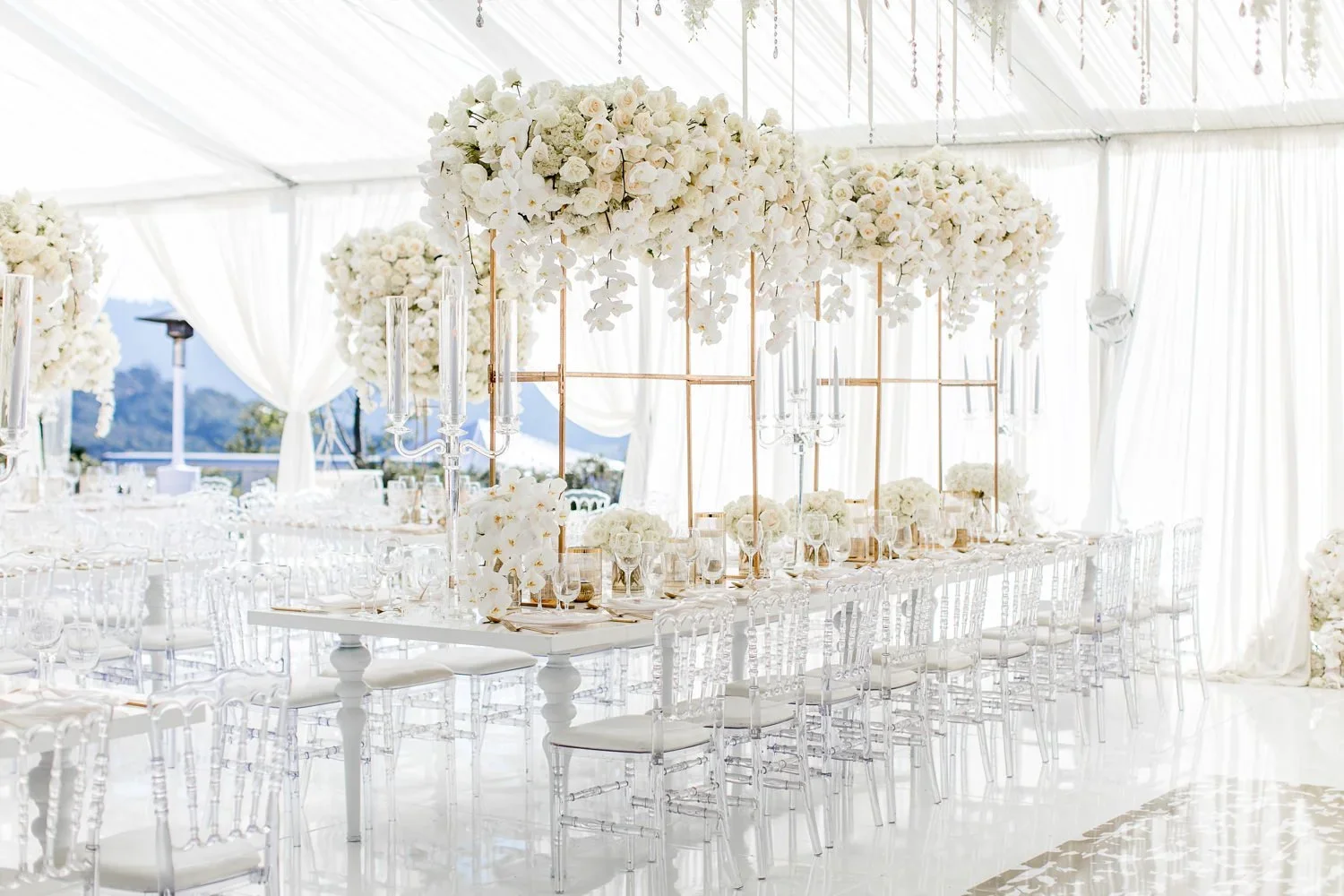 White floral installation and candelabras along a tented wedding reception table