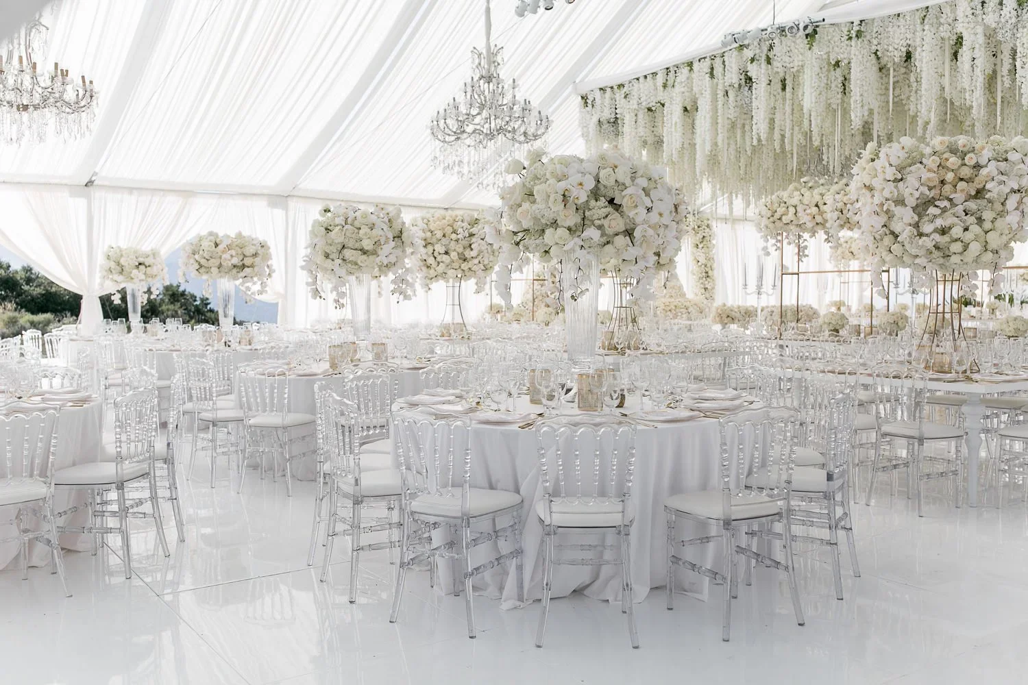 Crystal chandeliers over round tables at a white and gold wedding reception