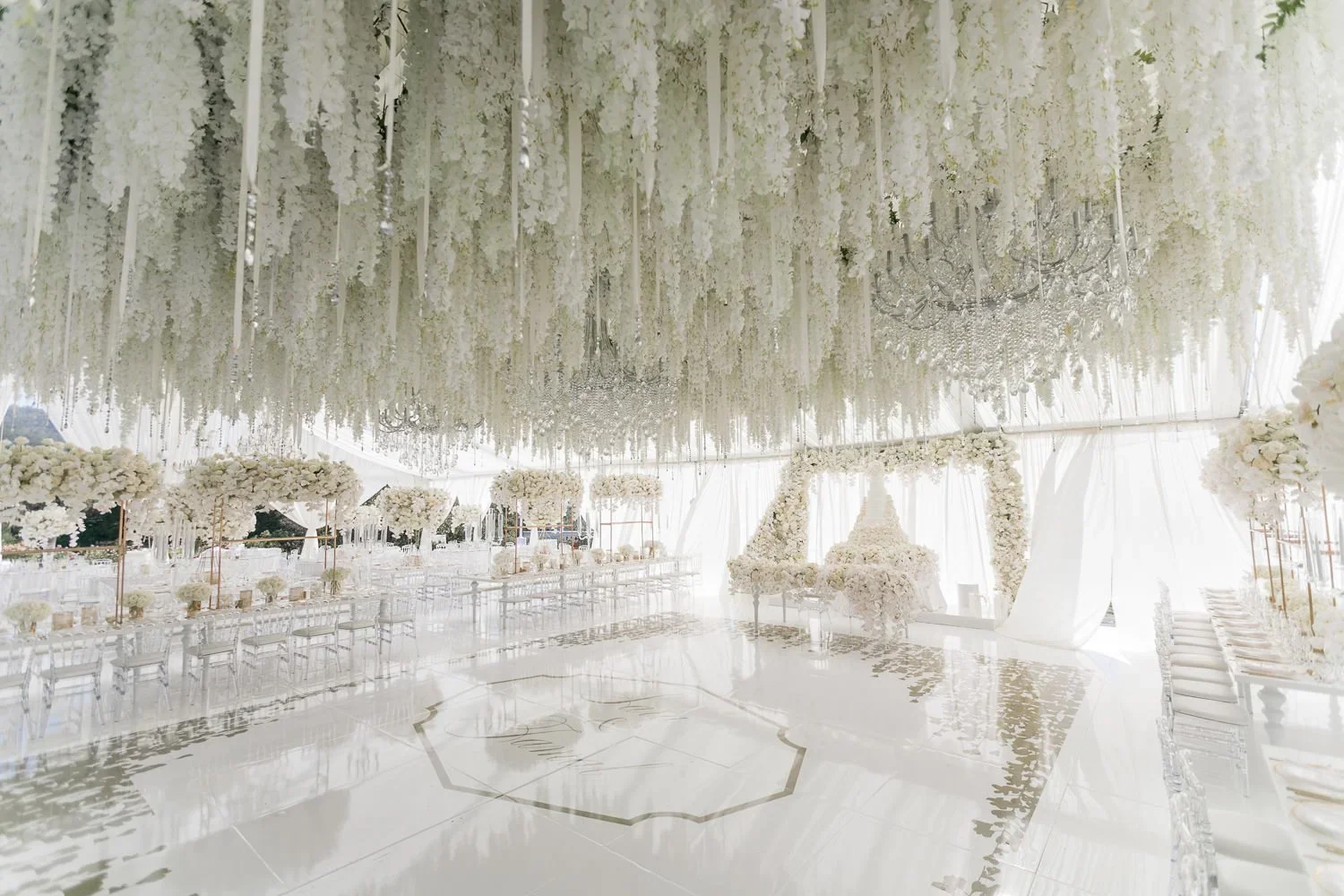 Tented wedding reception dance floor with floral cake backdrop in view