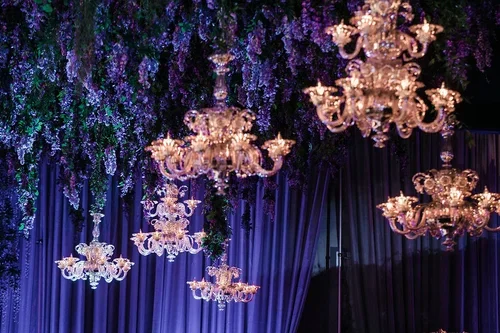 Crystal chandeliers beneath a purple wedding theme wisteria ceiling