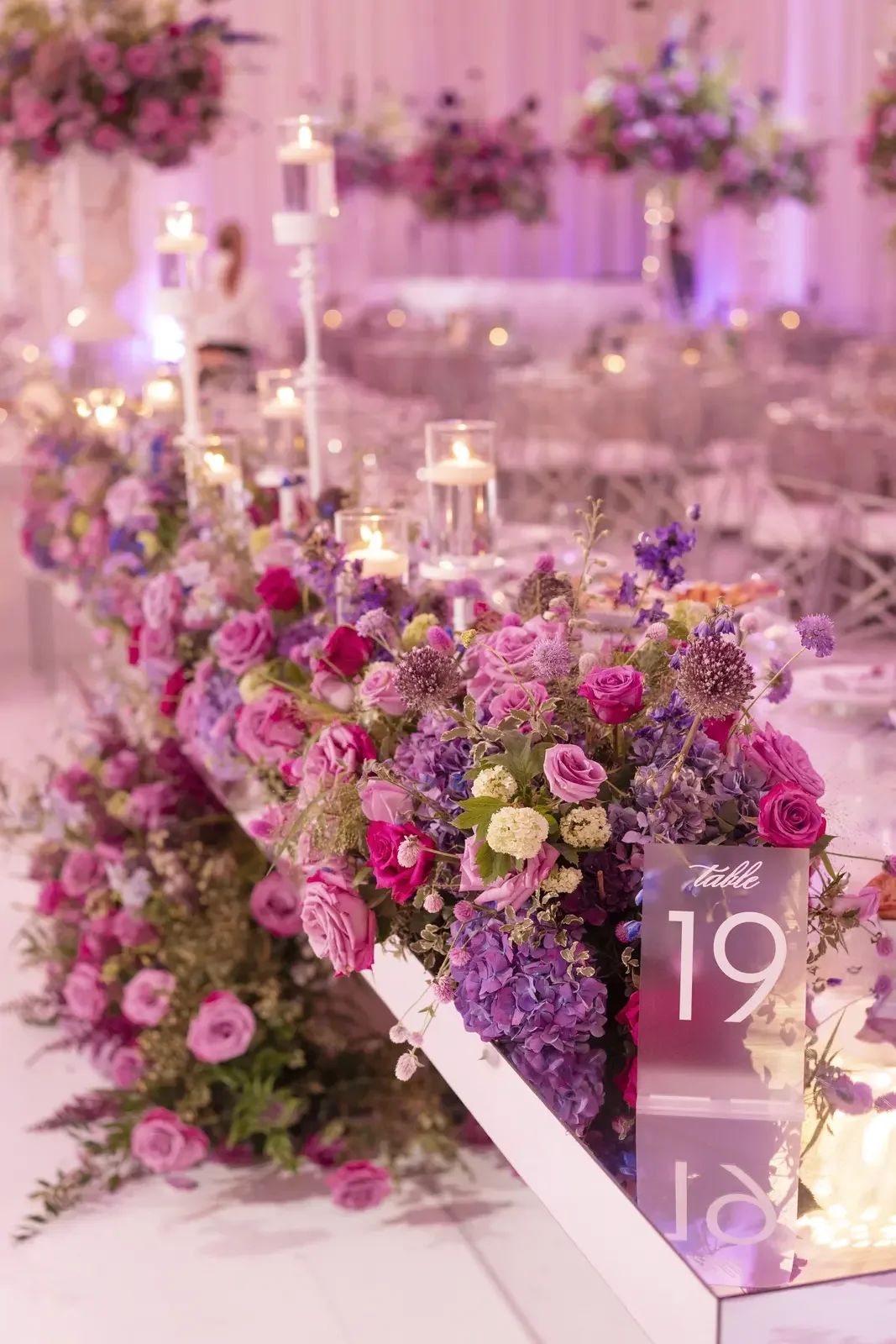 Pink and purple wedding flowers table runner with candles and table number