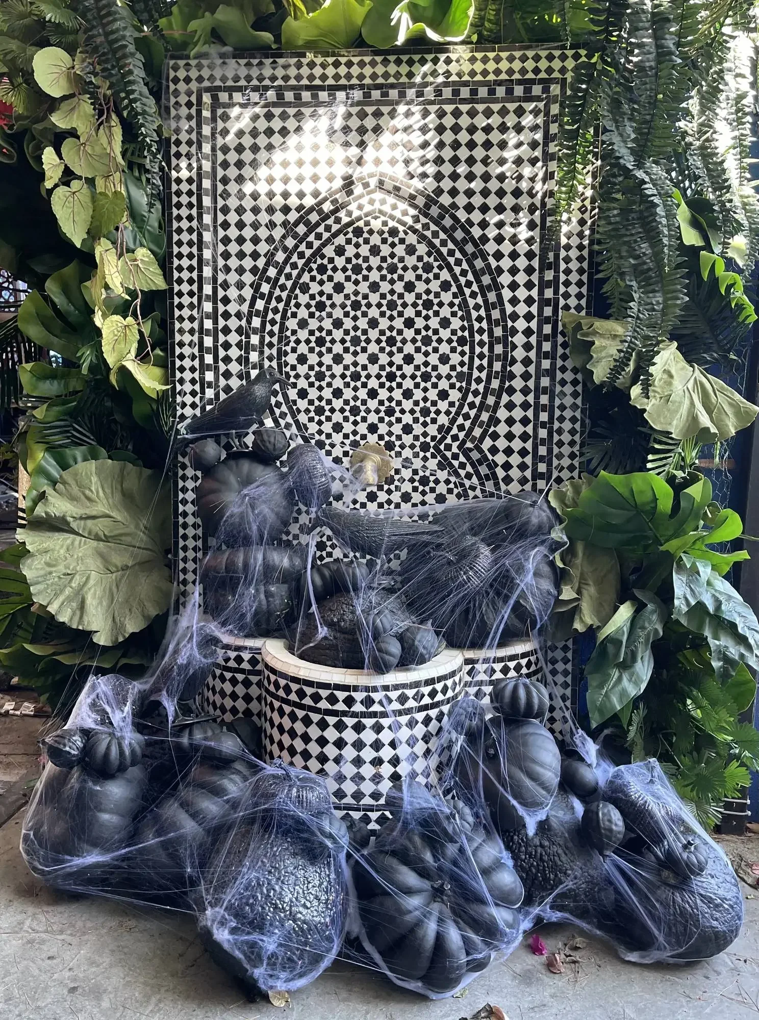 Luxury Halloween decor with black pumpkins, ravens and cobwebs around a mosaic fountain, by Eddie Zaratsian's Halloween decorators in Los Angeles