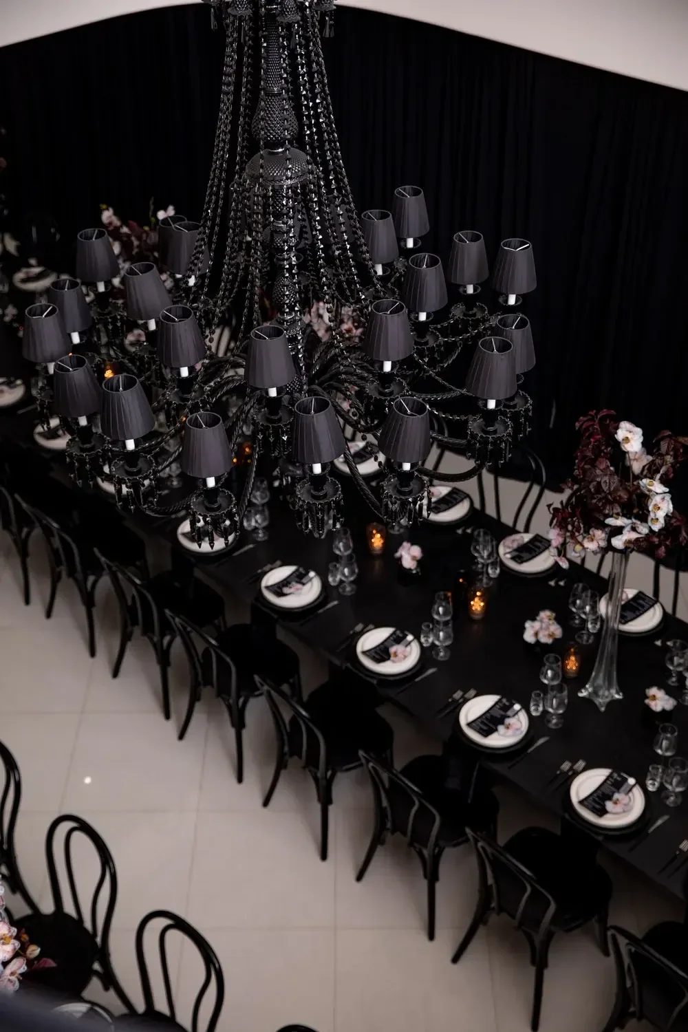 Black chandelier suspended over a long black dining table, part of a birthday event produced by a party planner